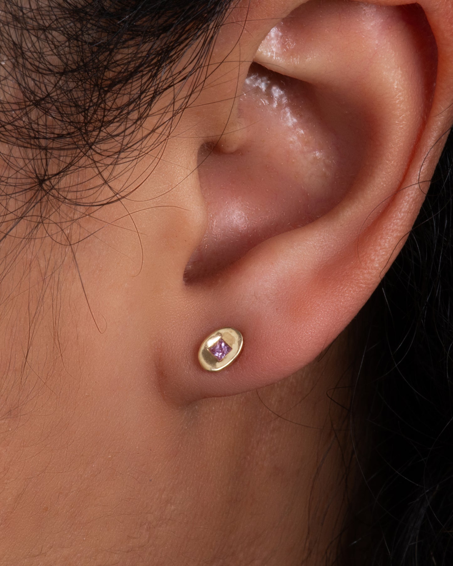 Yellow gold oval studs with princess cut pink sapphires. Shown on an ear.