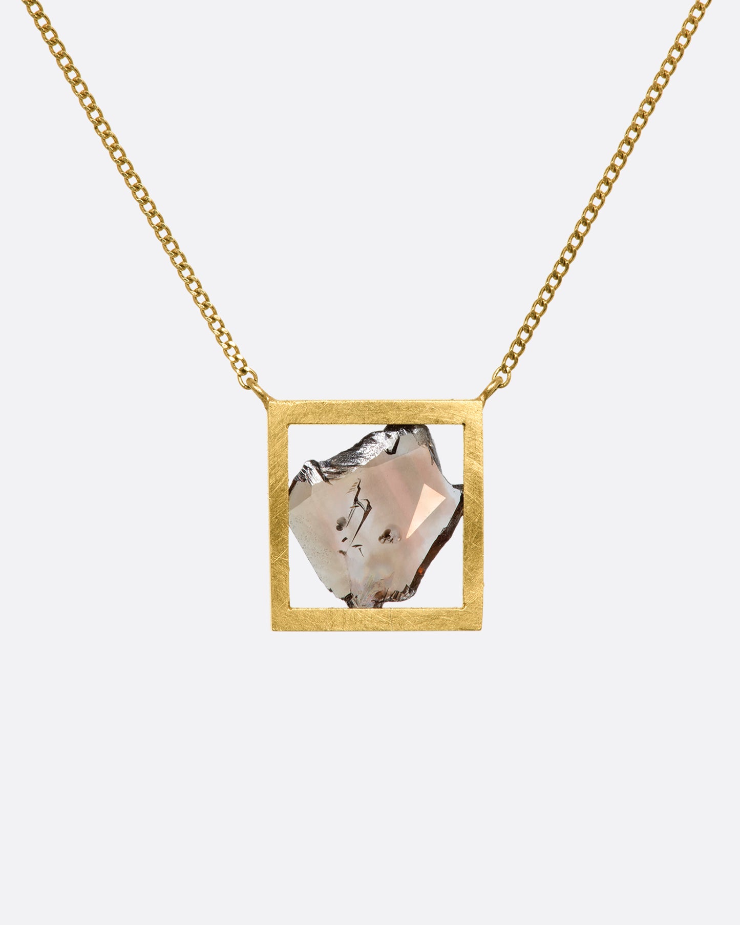 This dusky freeform diamond slice is thoughtfully framed in an open, warm yellow gold window. Suspended from a fine cable chain, this clean, minimalist fixed setting creates a cool, modern look. View from the front.