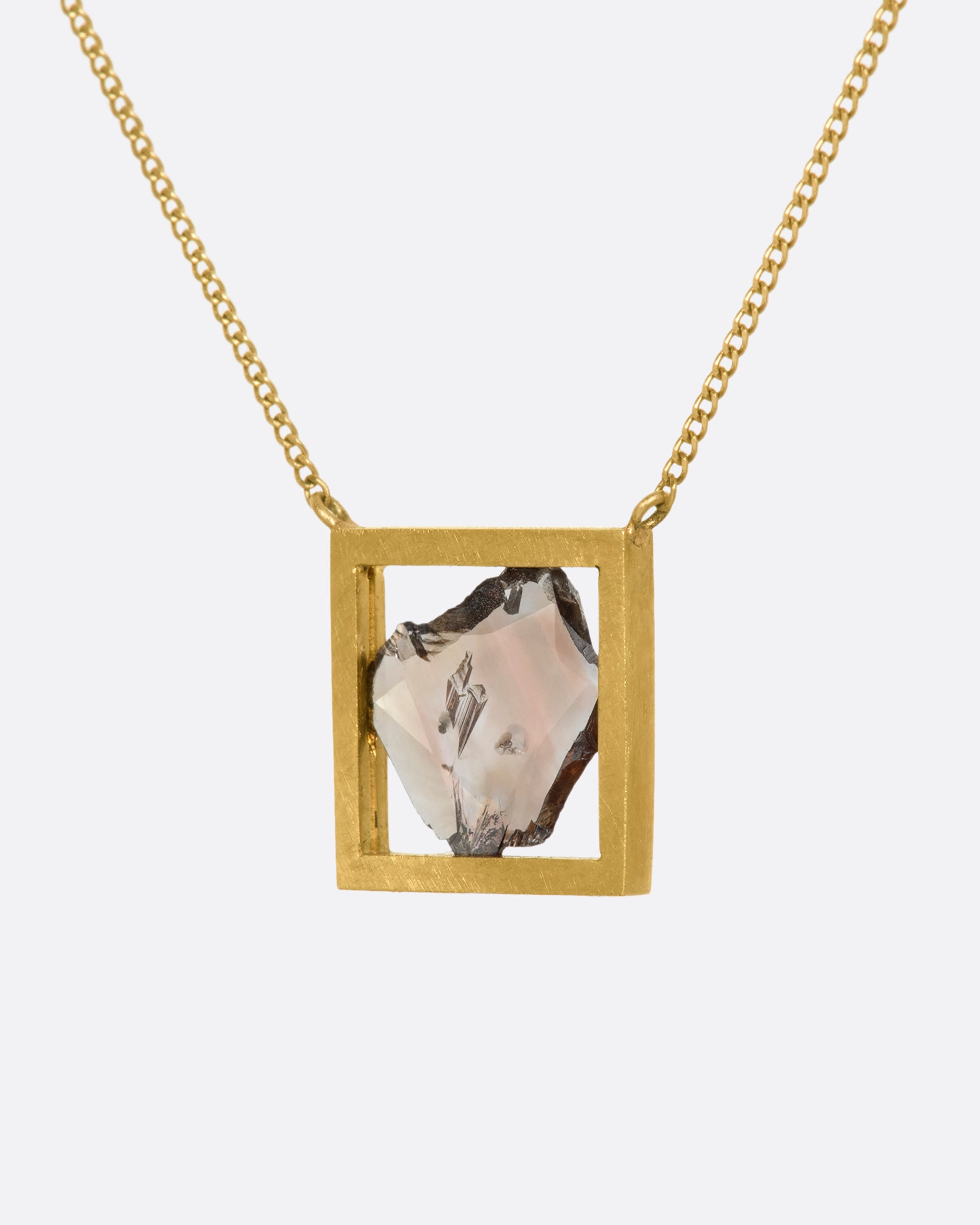 This dusky freeform diamond slice is thoughtfully framed in an open, warm yellow gold window. Suspended from a fine cable chain, this clean, minimalist fixed setting creates a cool, modern look. View from the side.