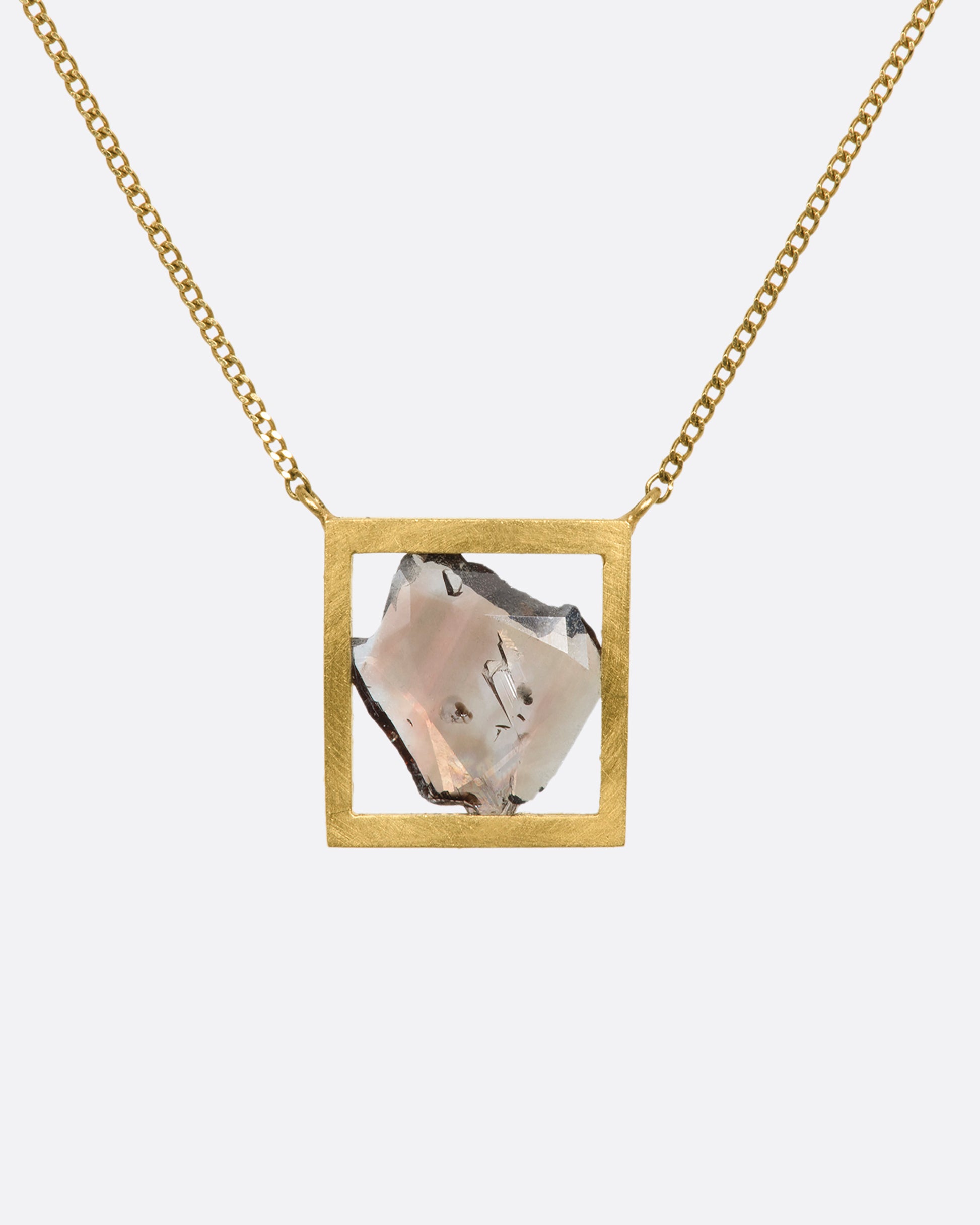 This dusky freeform diamond slice is thoughtfully framed in an open, warm yellow gold window. Suspended from a fine cable chain, this clean, minimalist fixed setting creates a cool, modern look. View from the back.