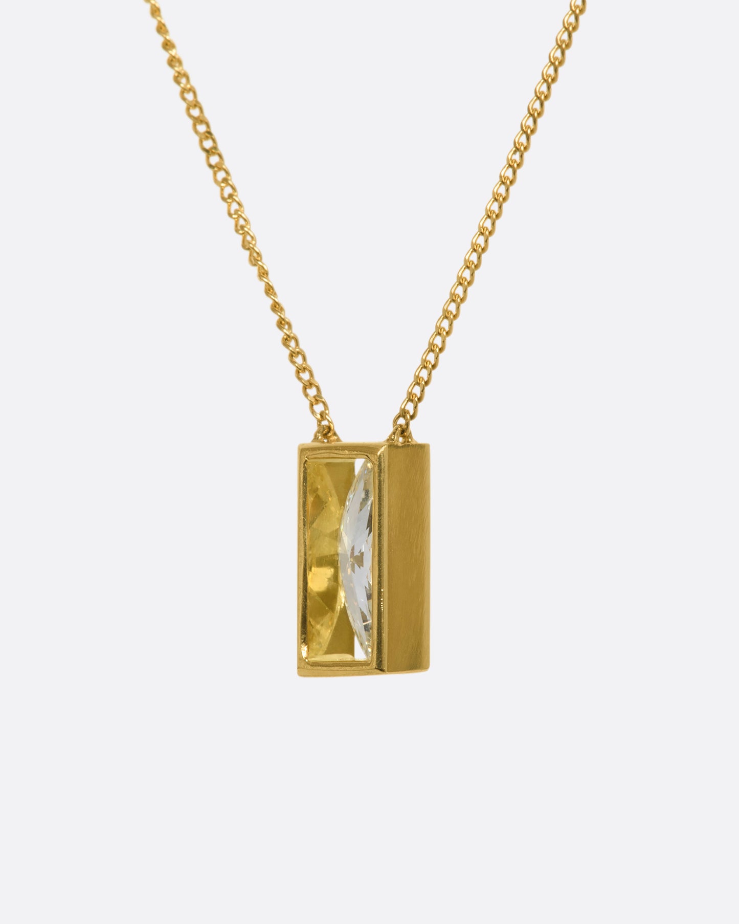 A brilliant marquise diamond throws sparkle from every angle as it hovers in an open, rich yellow gold fixed window. This minimalist setting is suspended from a fine yellow gold curb chain. View from the side.