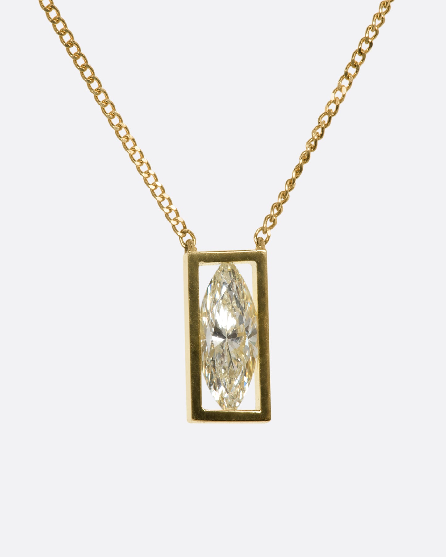 A brilliant marquise diamond throws sparkle from every angle as it hovers in an open, rich yellow gold fixed window. This minimalist setting is suspended from a fine yellow gold curb chain. View from the front.