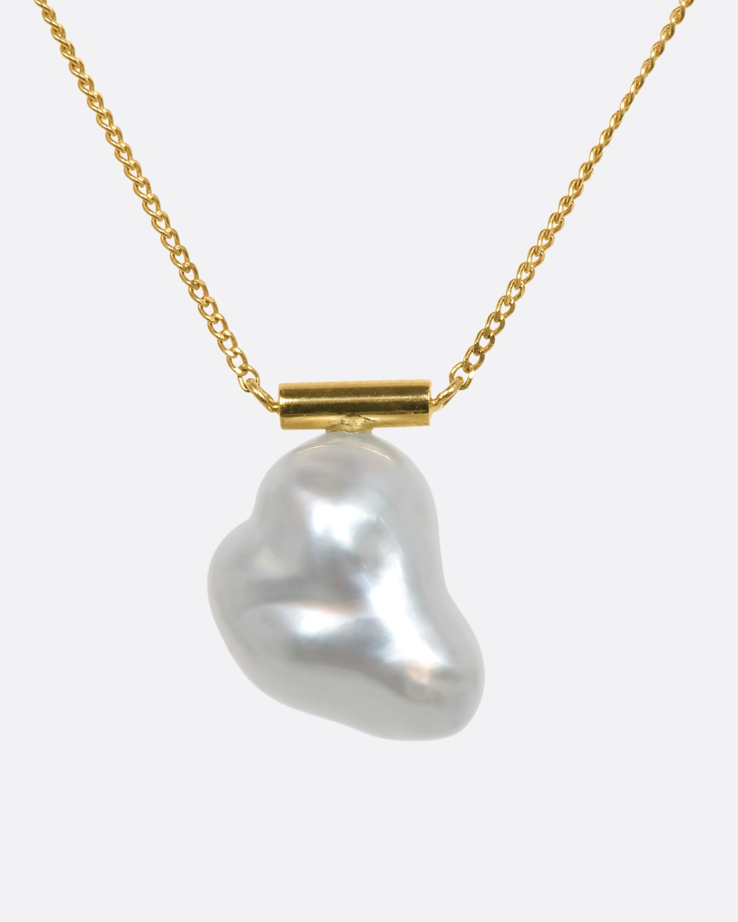 A freeform South Sea baroque pearl is suspended from a minimalist gold bar and fine yellow gold cable chain. The beautiful, natural curvature of this rare pearl allows light to reflect in a multitude of paths, glowing from every angle.