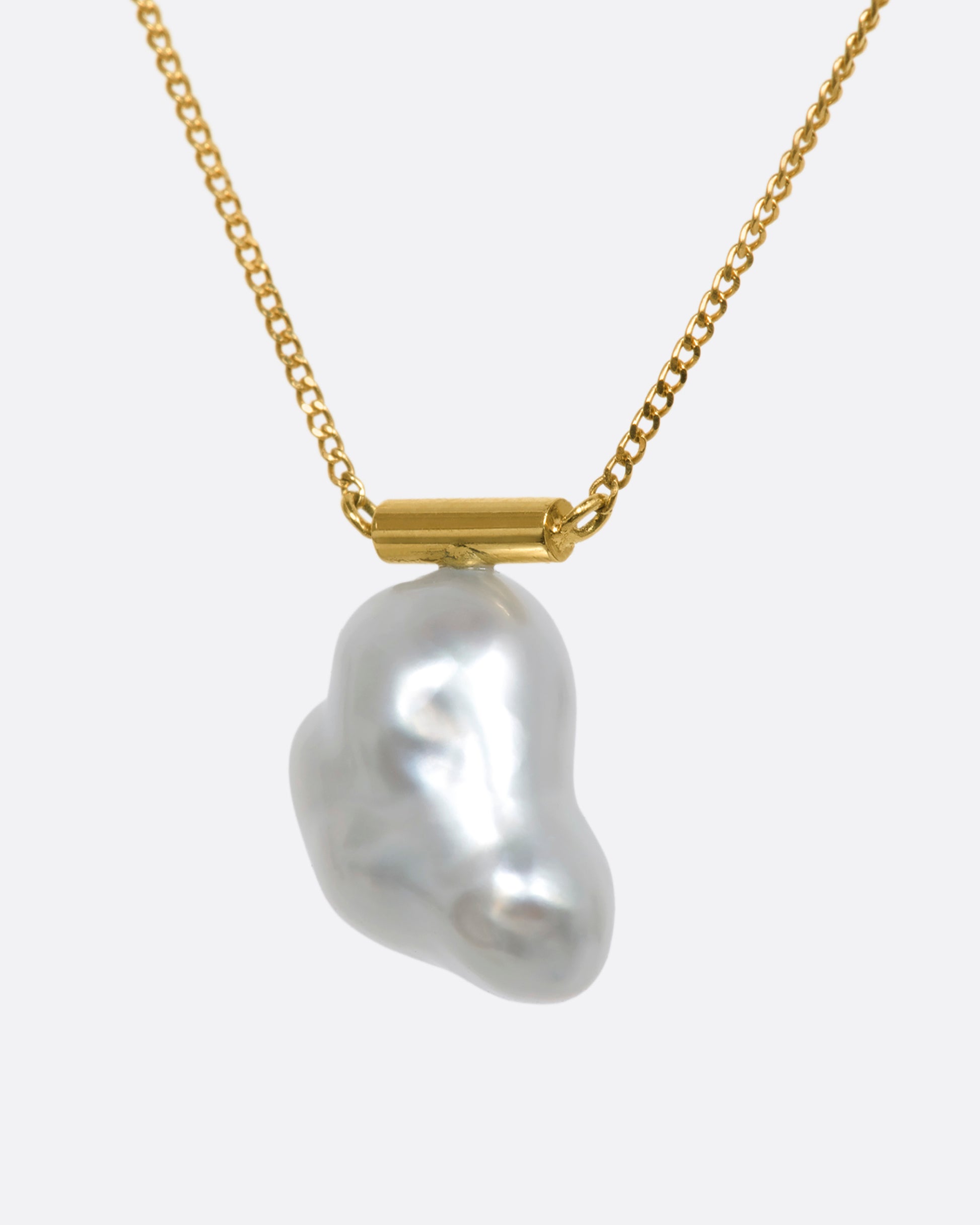 A freeform South Sea baroque pearl is suspended from a minimalist gold bar and fine yellow gold cable chain. The beautiful, natural curvature of this rare pearl allows light to reflect in a multitude of paths, glowing from every angle.