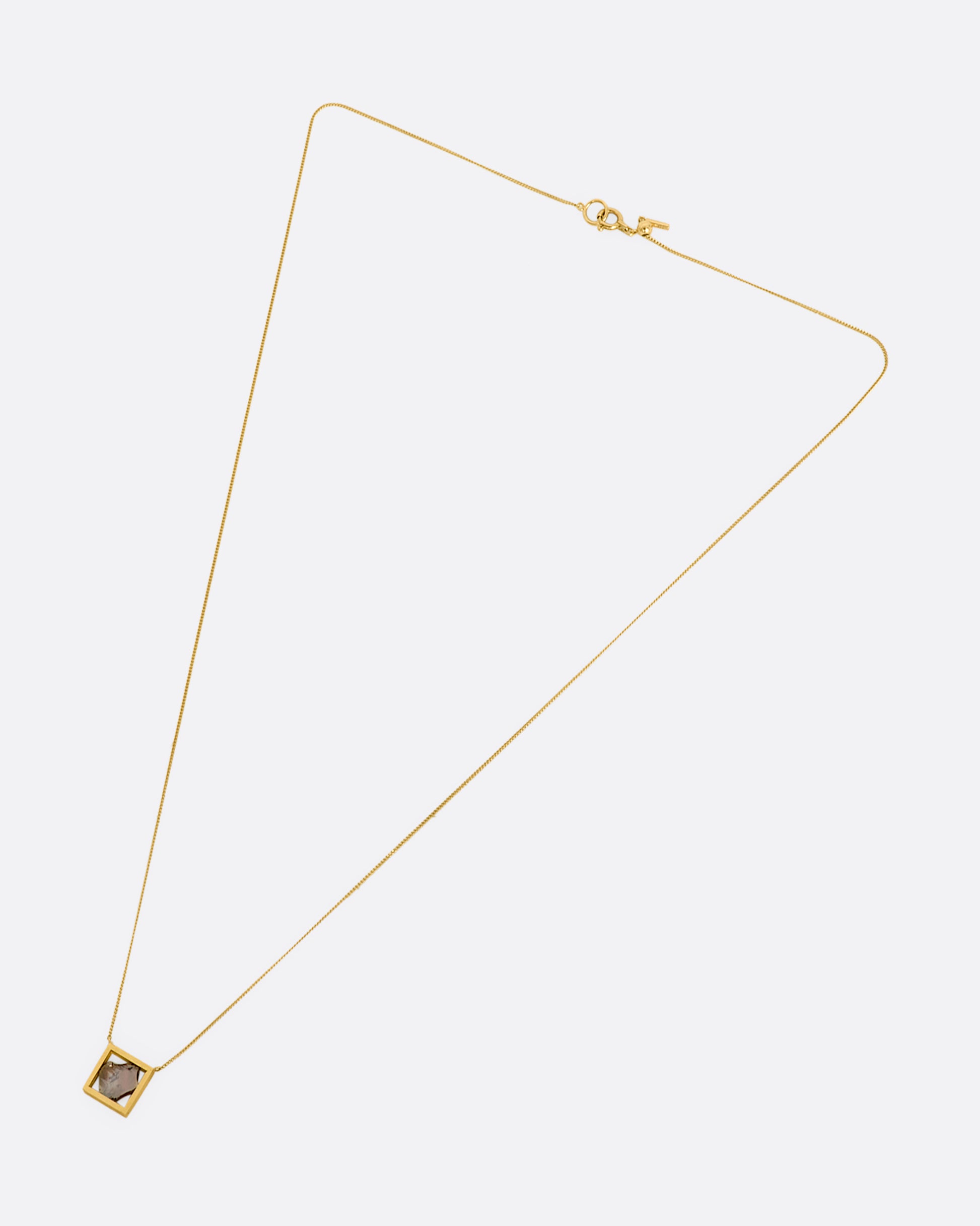 This dusky freeform diamond slice is thoughtfully framed in an open, warm yellow gold window. Suspended from a fine cable chain, this clean, minimalist fixed setting creates a cool, modern look. View laying flat from above.