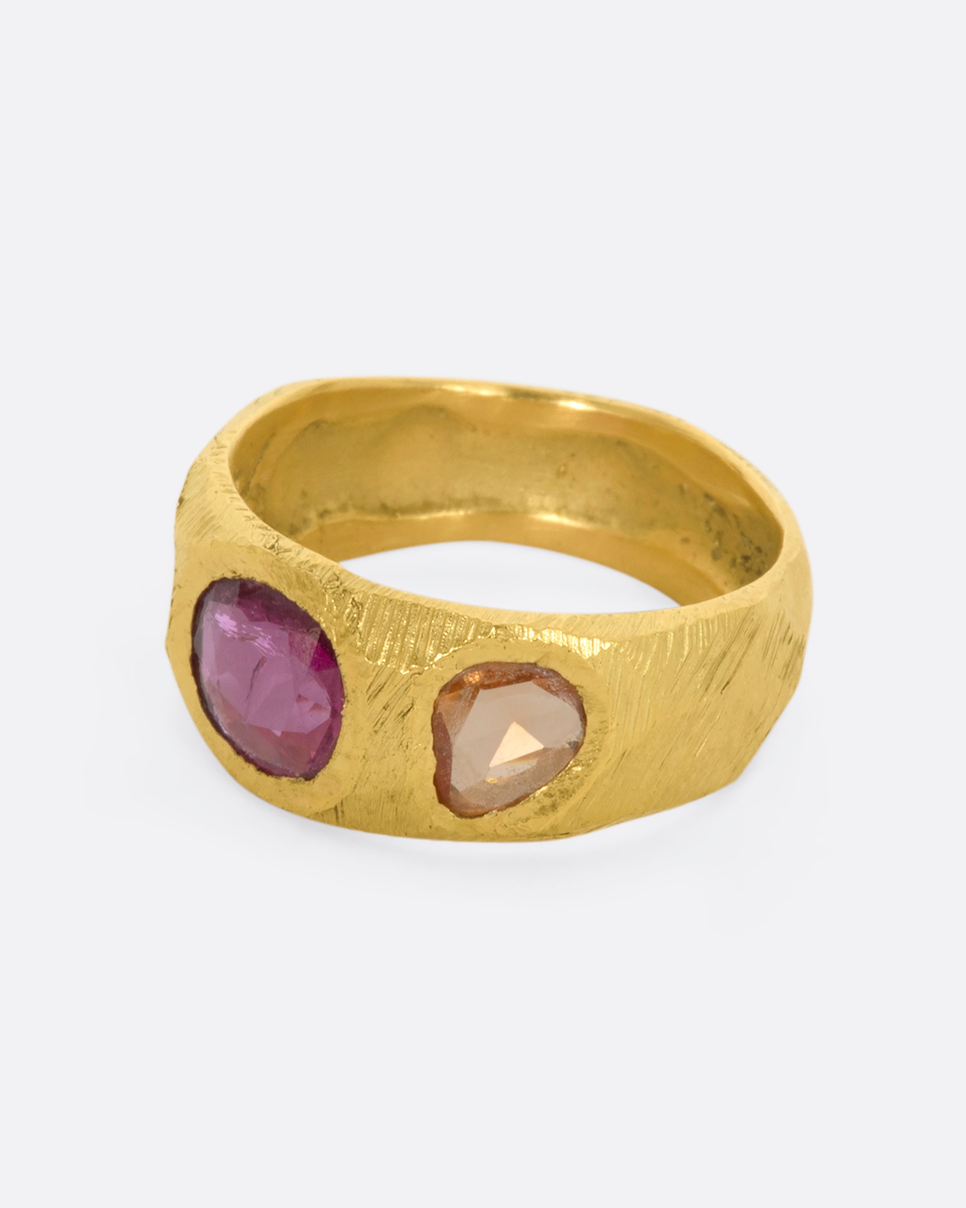 A yellow gold band with three large sapphires, one pink and two orange. Shown from the side.