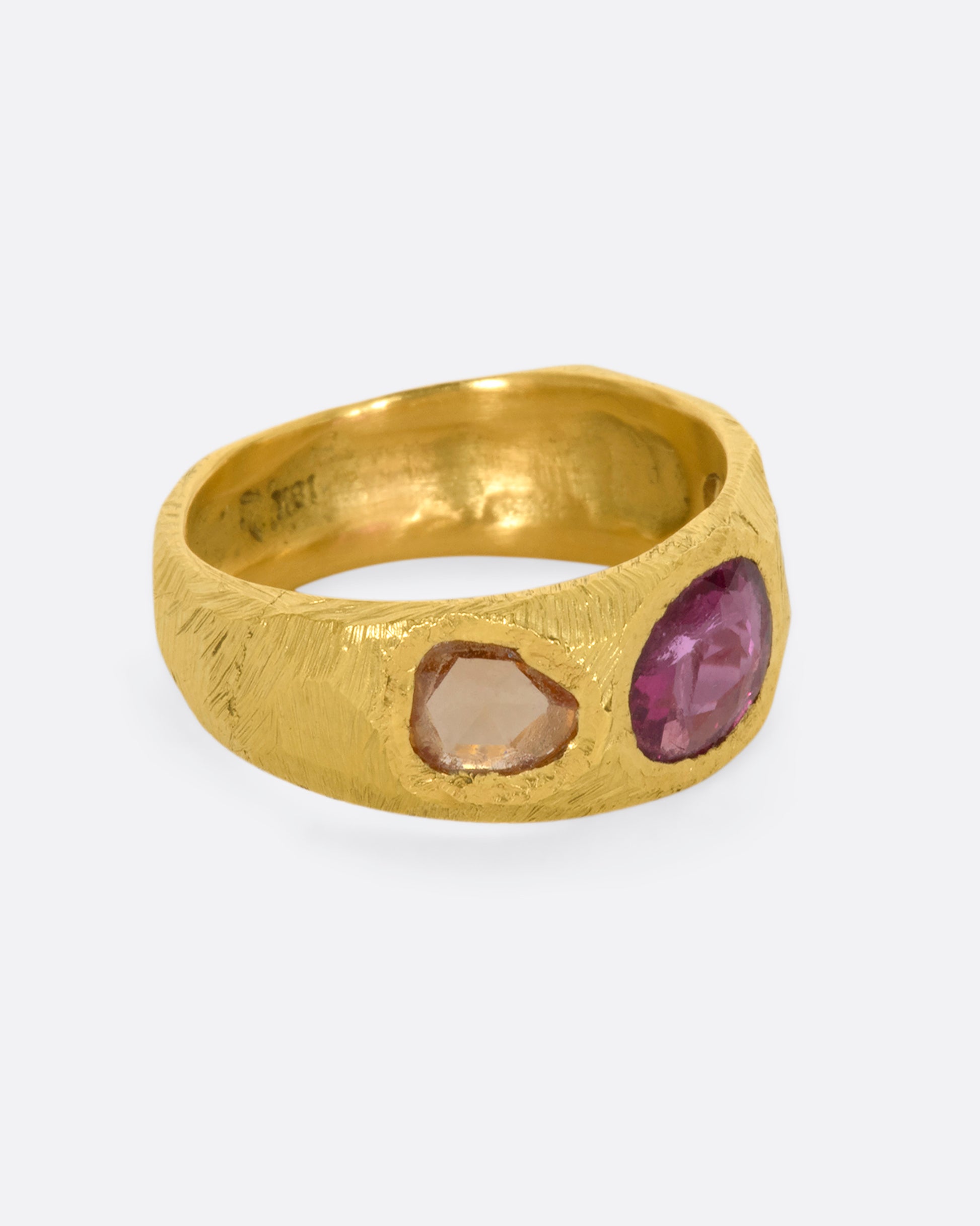 A yellow gold band with three large sapphires, one pink and two orange. Shown from the side.