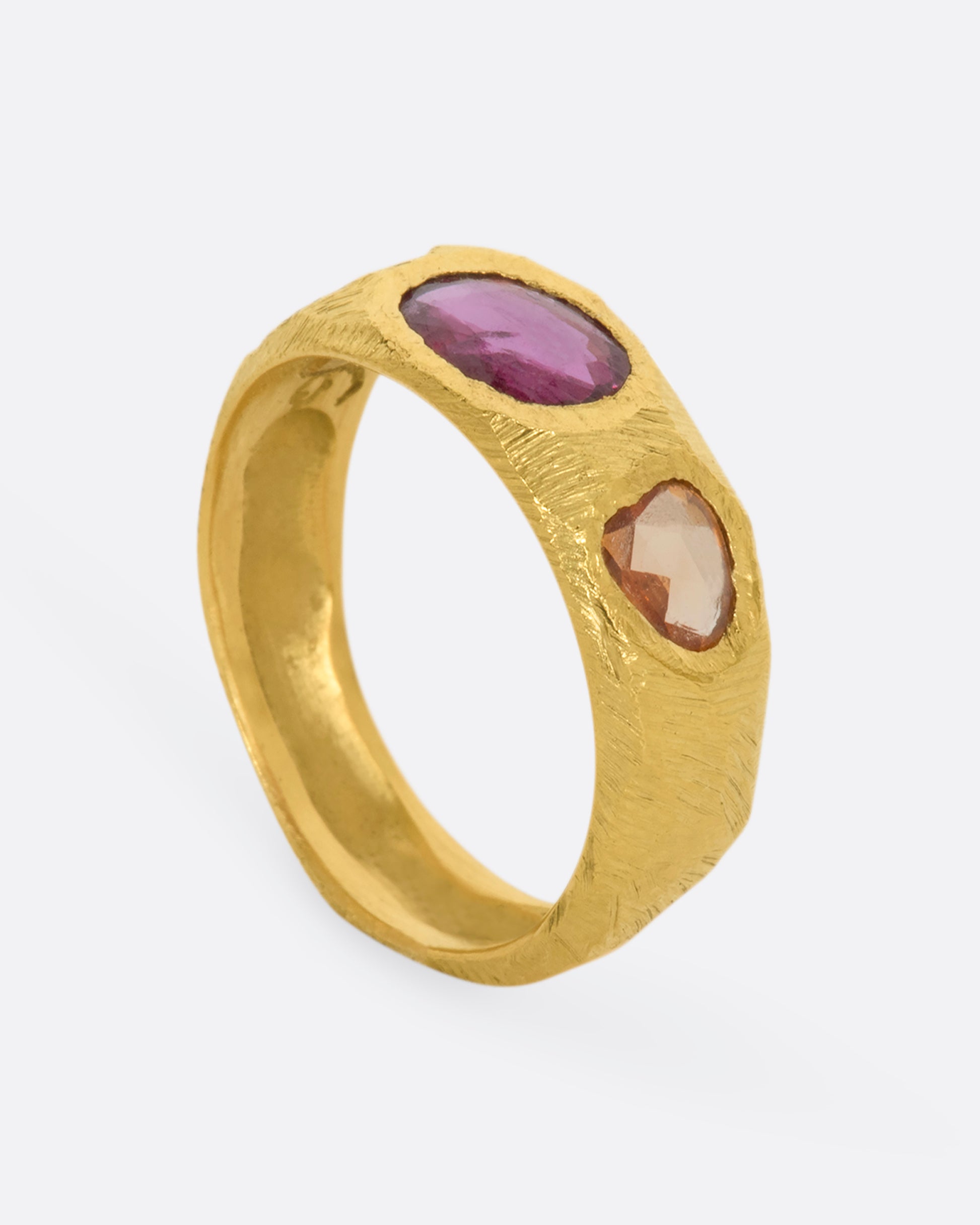 A yellow gold band with three large sapphires, one pink and two orange. Shown from the side, standing up.