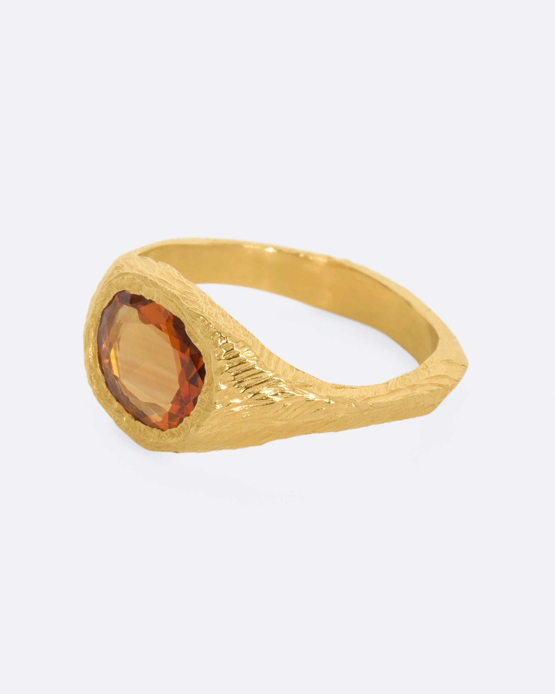 A hand carved yellow gold ring with an orange sapphire. View from the side.