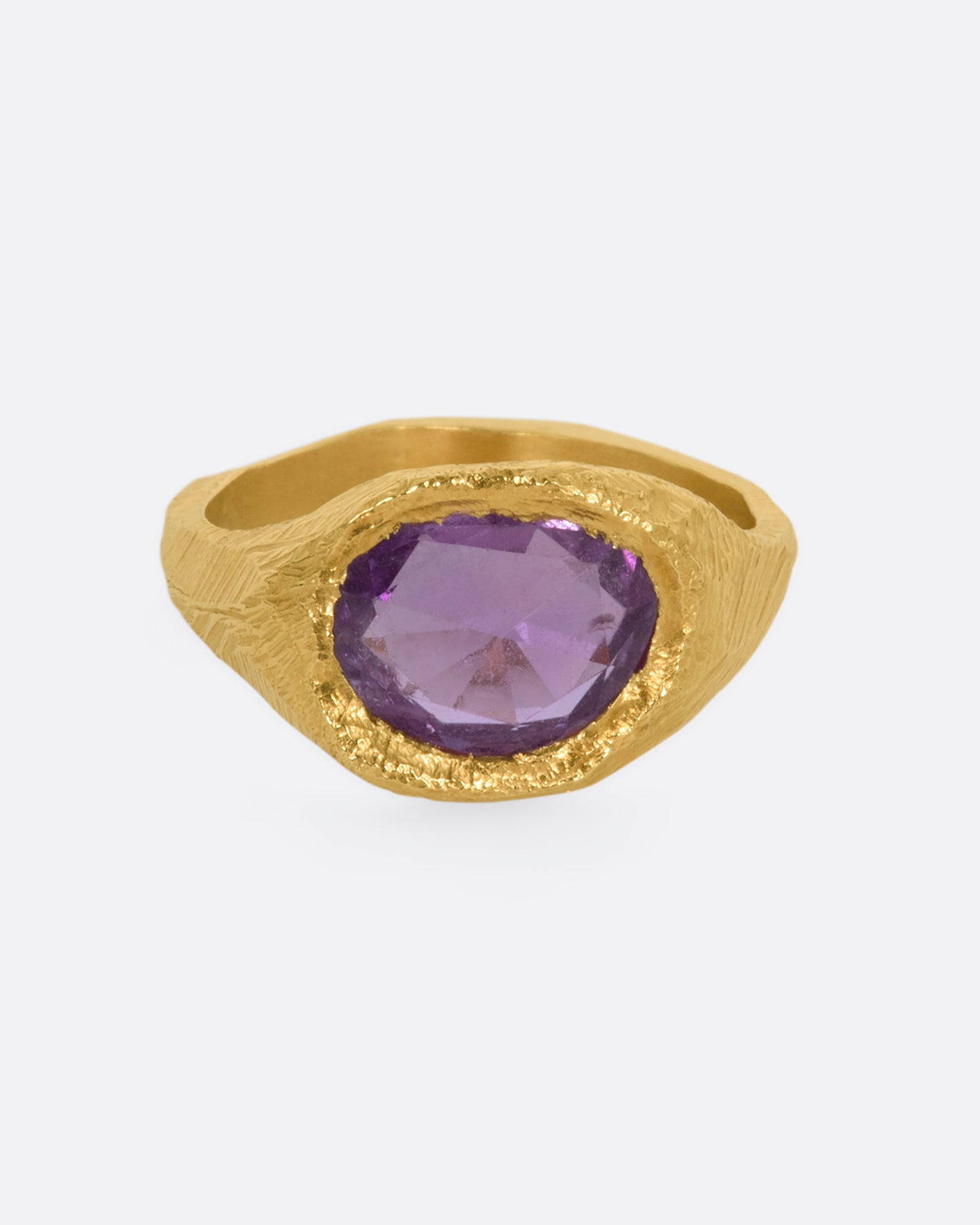 A textured yellow gold signet style ring with a rose cut purple sapphire. View from the front.