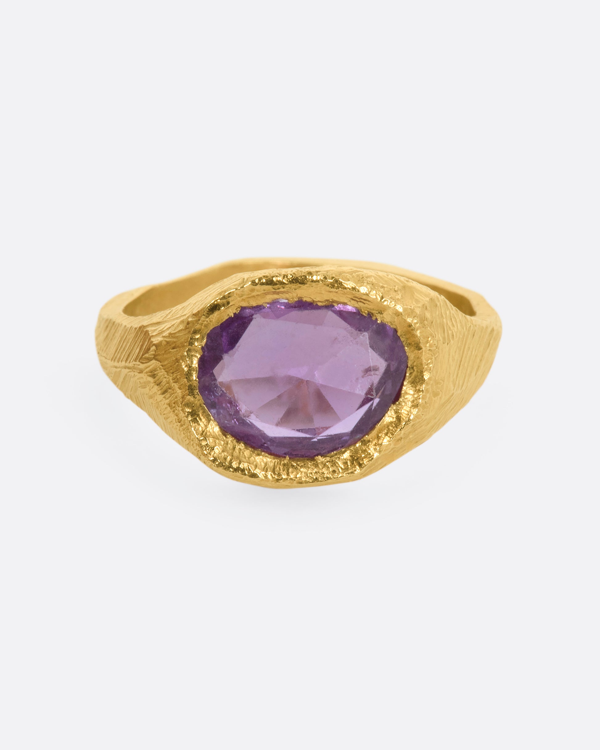 A textured yellow gold signet style ring with a rose cut purple sapphire. View from the front.