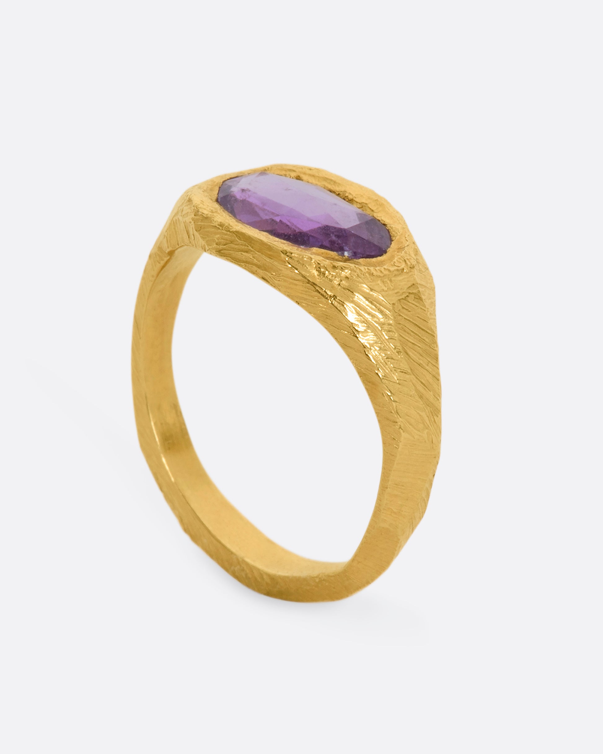 A textured yellow gold signet style ring with a rose cut purple sapphire. View standing.