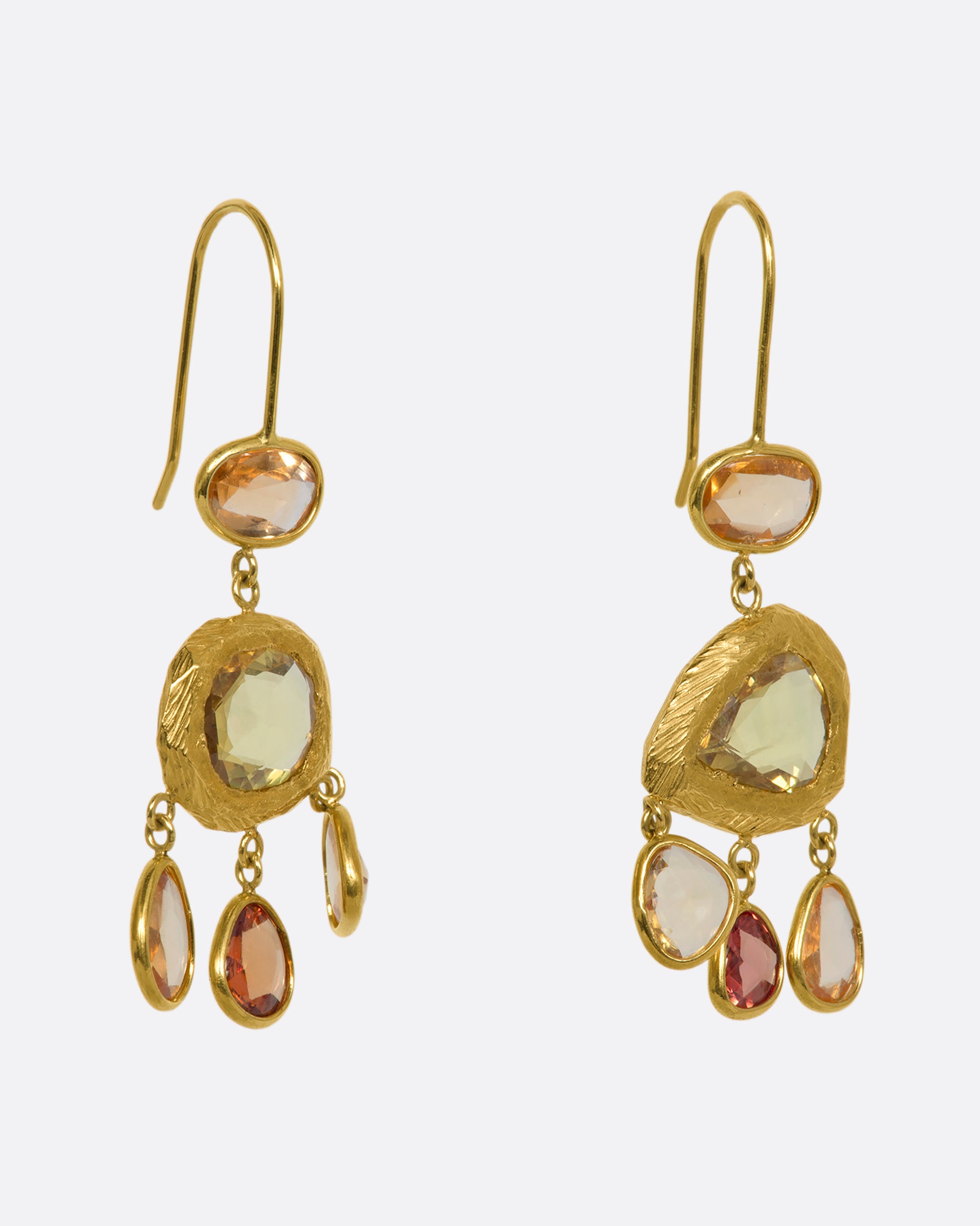 Yellow gold chandelier earrings with three orange sapphires dangling from the bottom. View from the side.