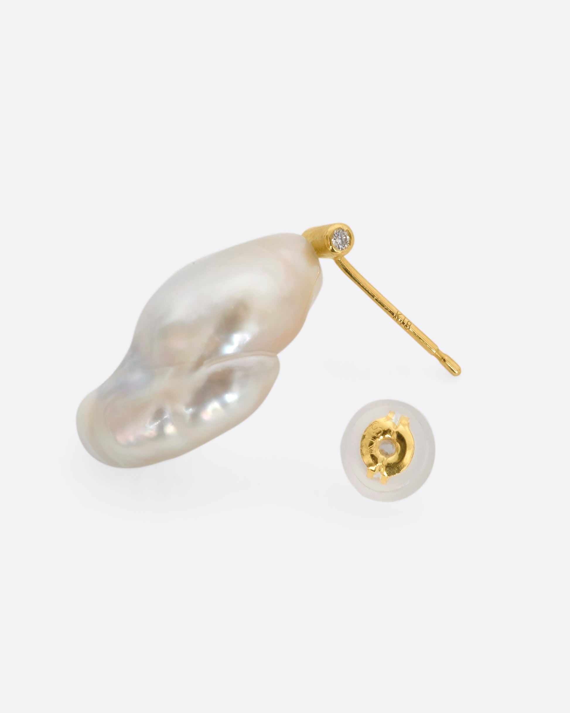 A large baroque pearl stud earring with a yellow gold bar containing diamonds on either end. View from the side including the backing.