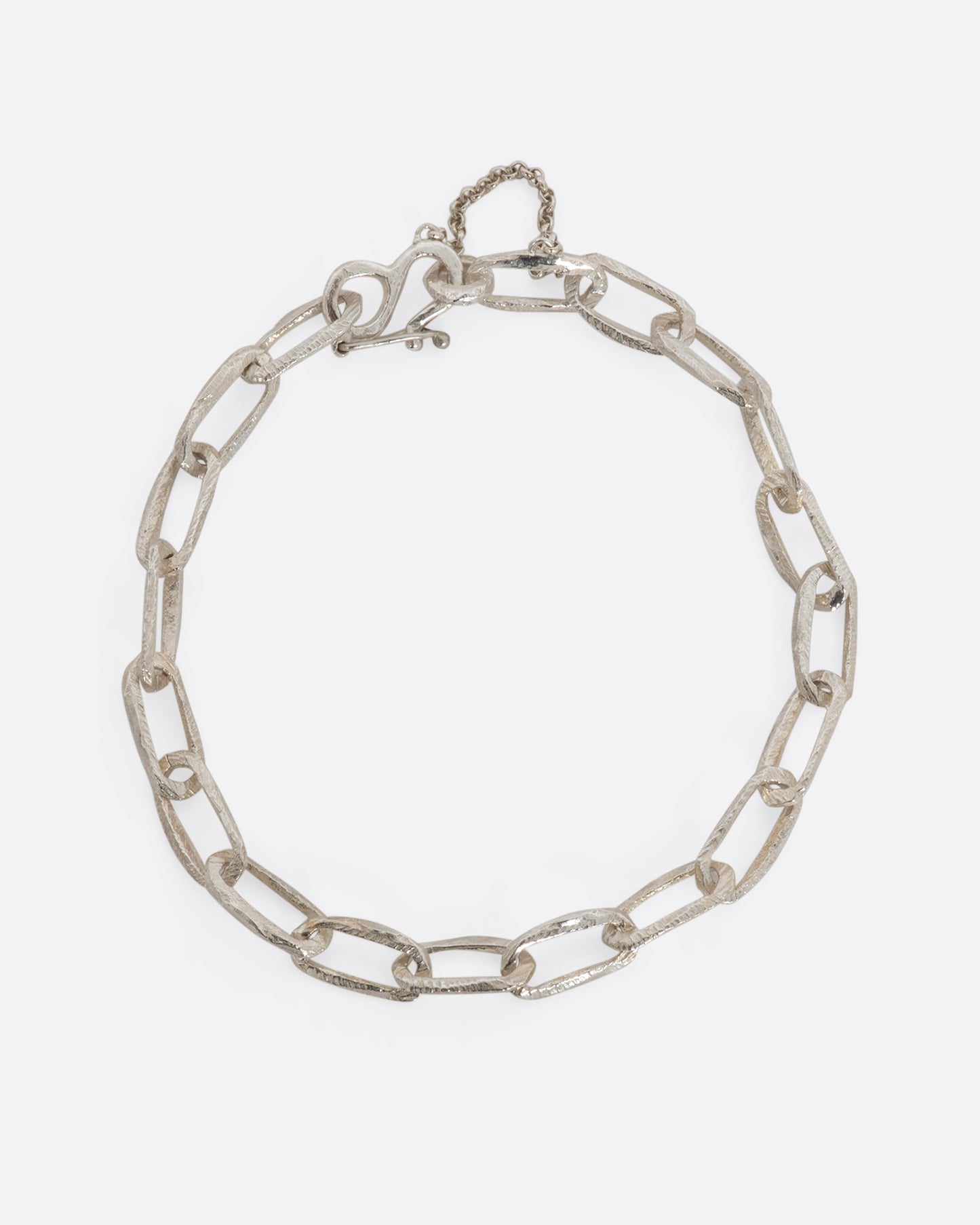 A sterling silver chain link bracelet with textured links and a safety chain. View closed, from above.