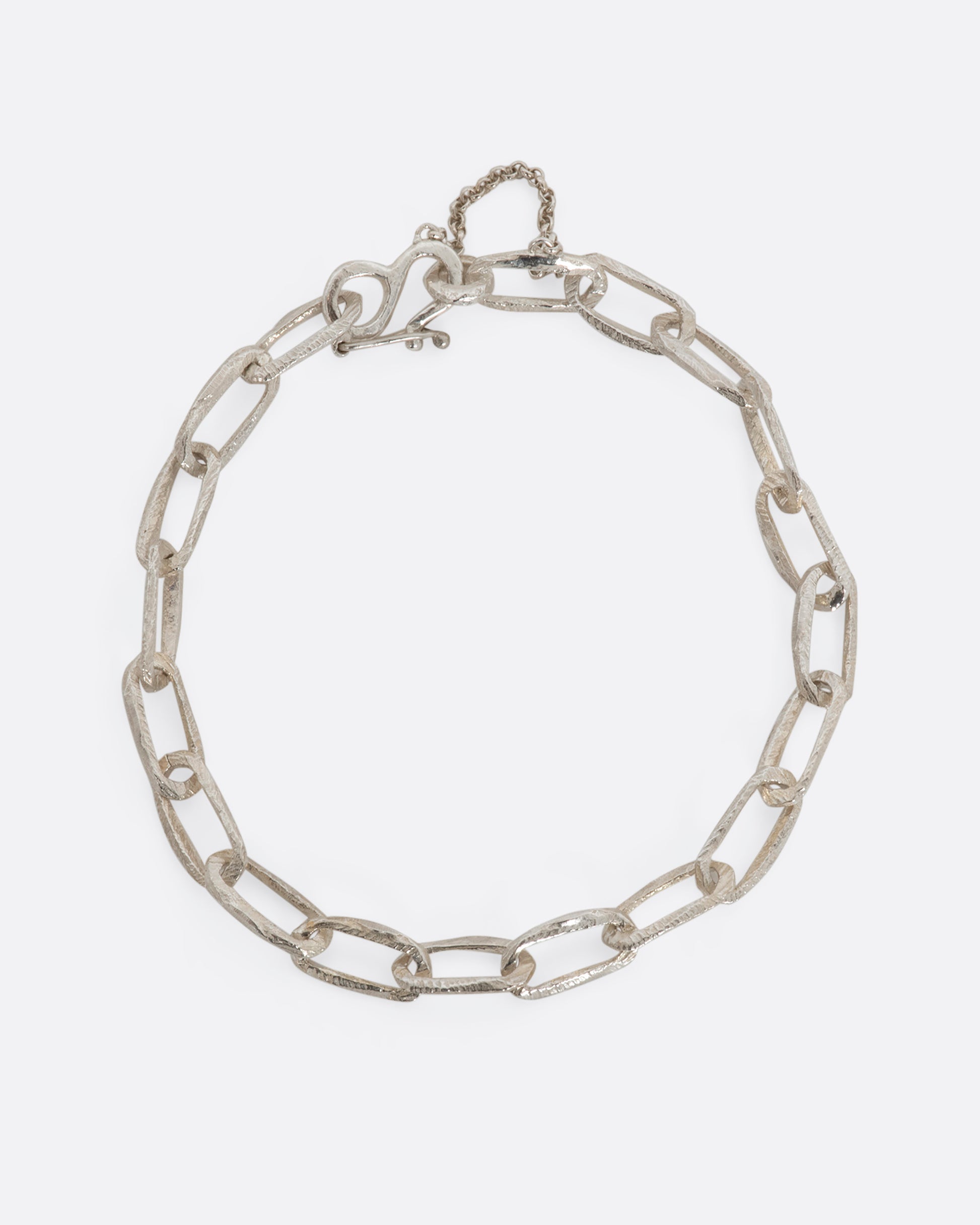 A sterling silver chain link bracelet with textured links and a safety chain. View closed, from above.