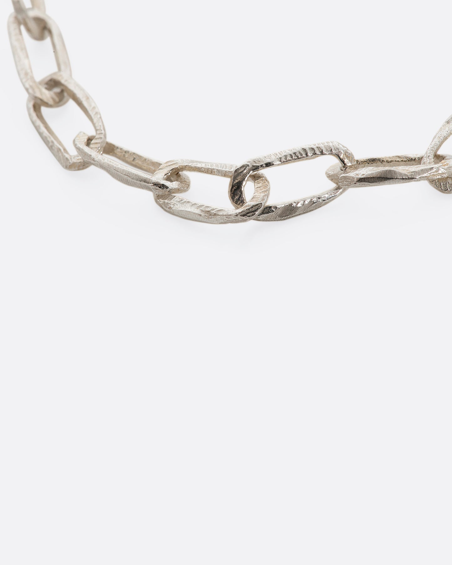 A sterling silver chain link bracelet with textured links and a safety chain. View up close of the links.