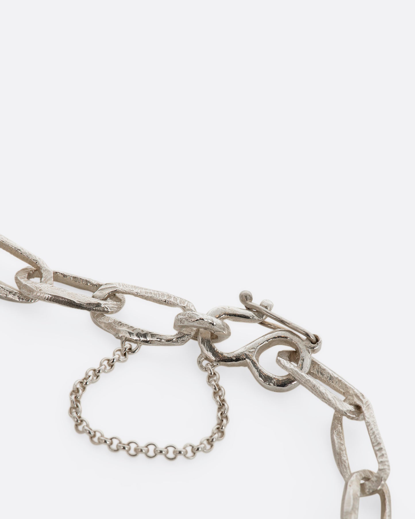 A sterling silver chain link bracelet with textured links and a safety chain. View of the closure close up.