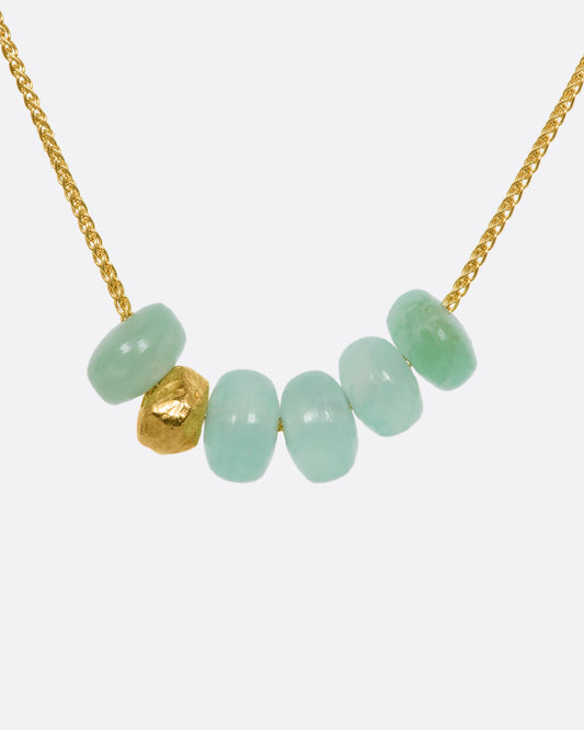 A yellow gold necklace with six beads, five of them chrysoprase and one of them textured gold. View close up from the front.