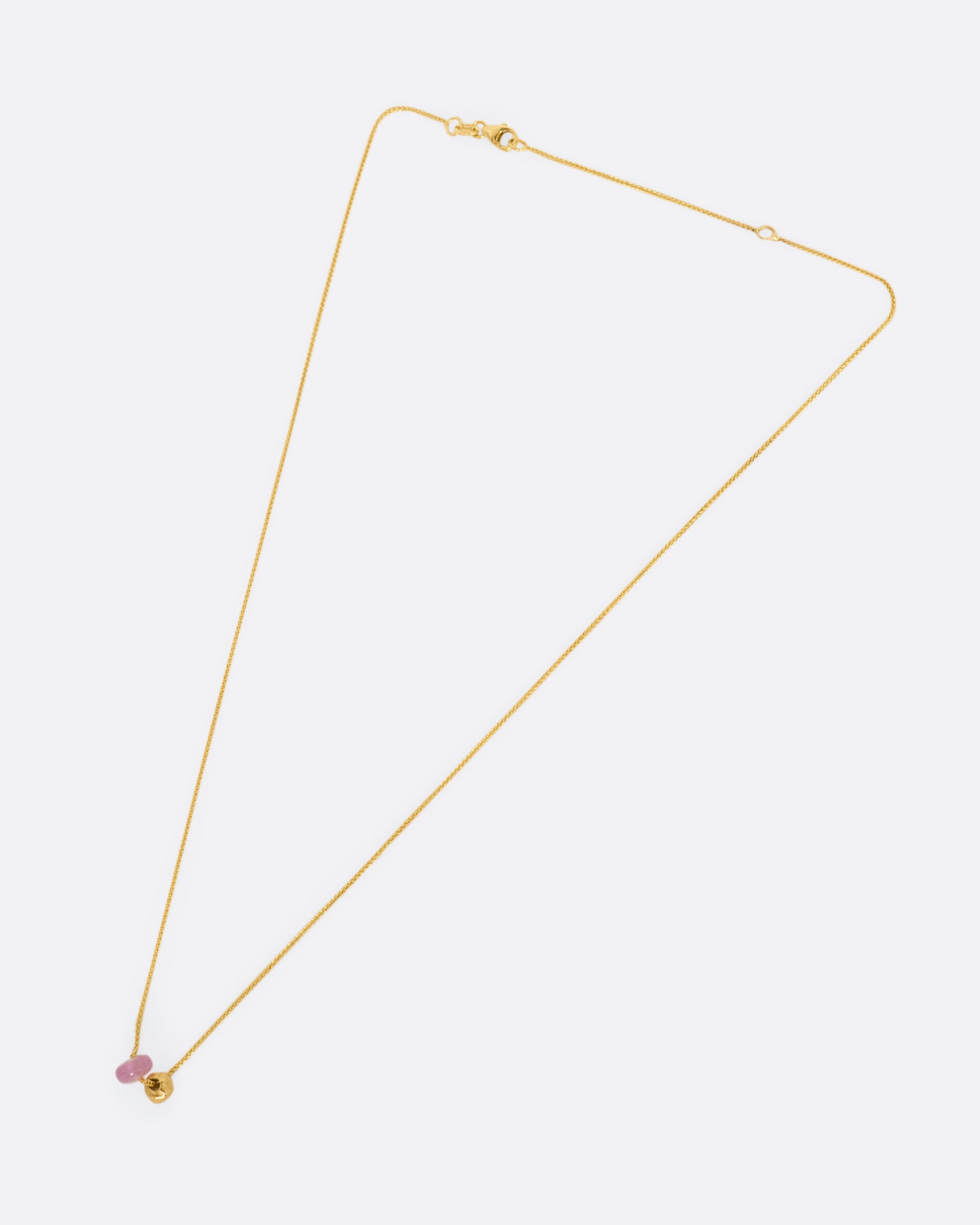 A pink tourmaline bead and gold textured bead hang from a yellow gold chain. View of the entire necklace from above.