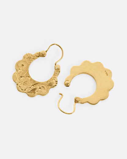 A pair of yellow gold hoop earrings with scalloped edges and floral details, shown from the side with one earring open.