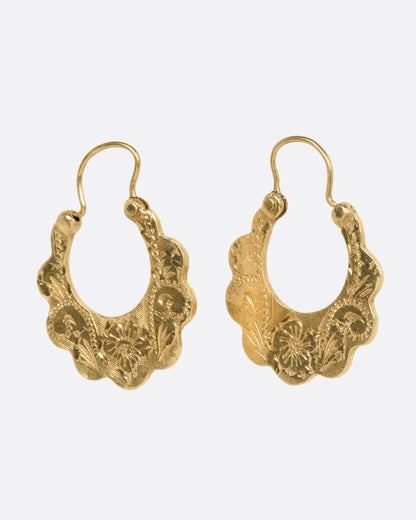 A pair of yellow gold hoop earrings with scalloped edges and floral details, shown from the side.