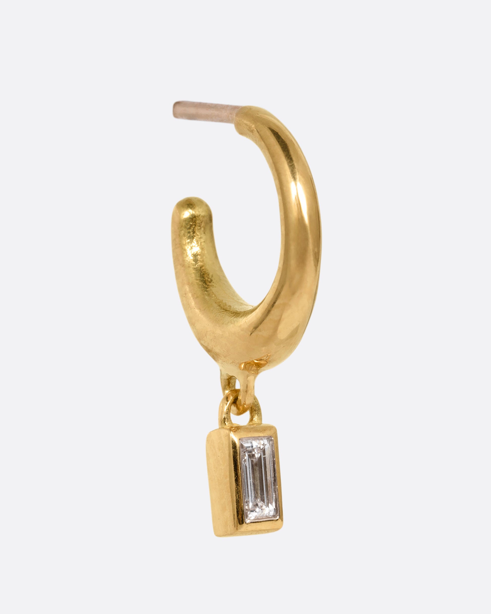 A yellow gold huggie hoop earring with a baguette diamond dangle. Shown from the side.