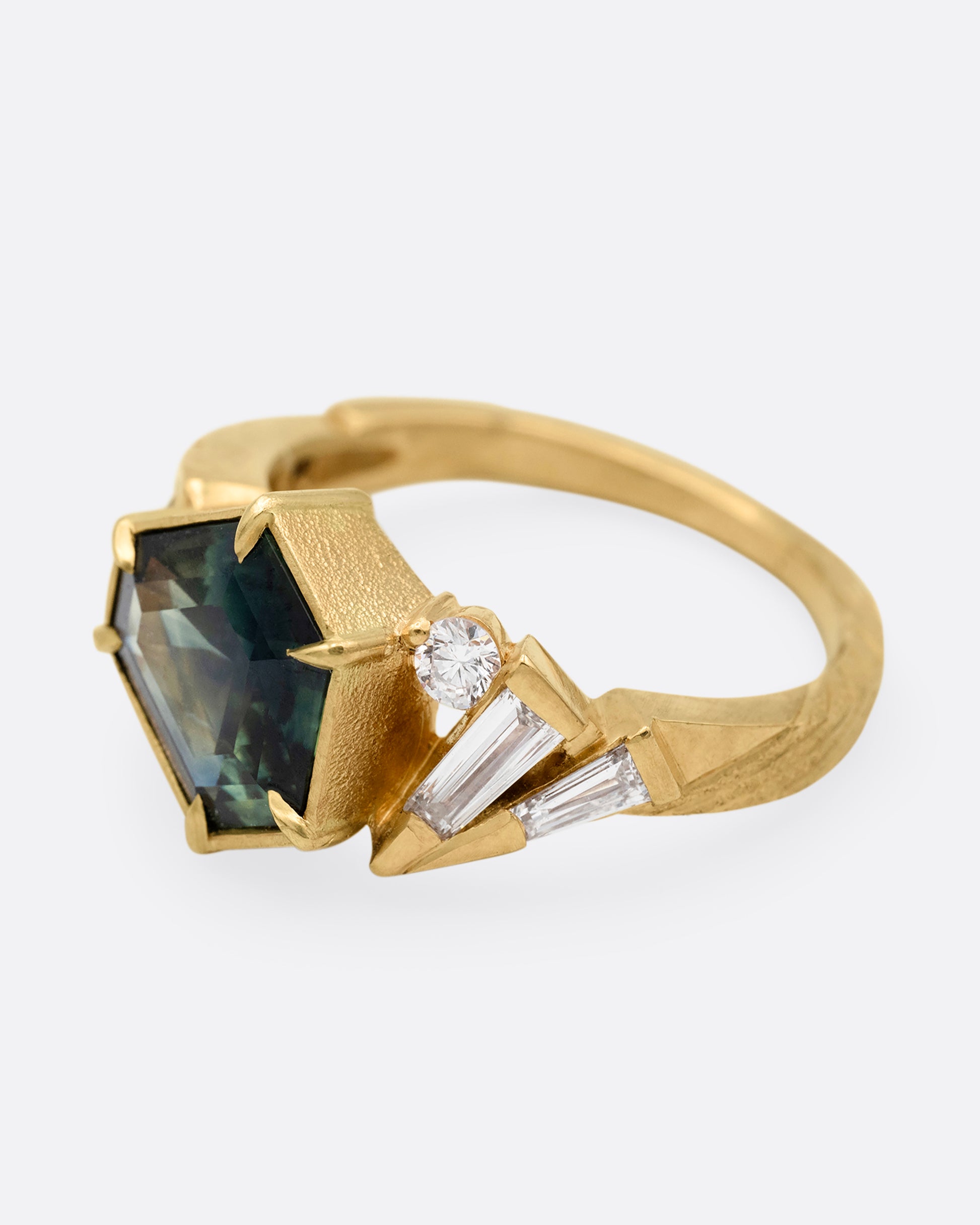 A yellow gold ring with a prong set Australian sapphire and white diamonds shown from the side.