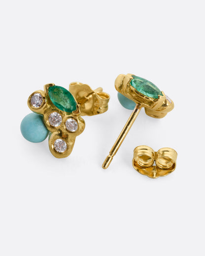 A pair of yellow gold stud earrings with diamonds, emeralds, and turquoise. One earring is shown from the front, the other is shown open from the back.