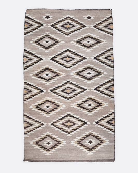A bird's eye view of a tan, black, and white Navajo Diamond Eye Dazzler rug with a serrated diamond motif.