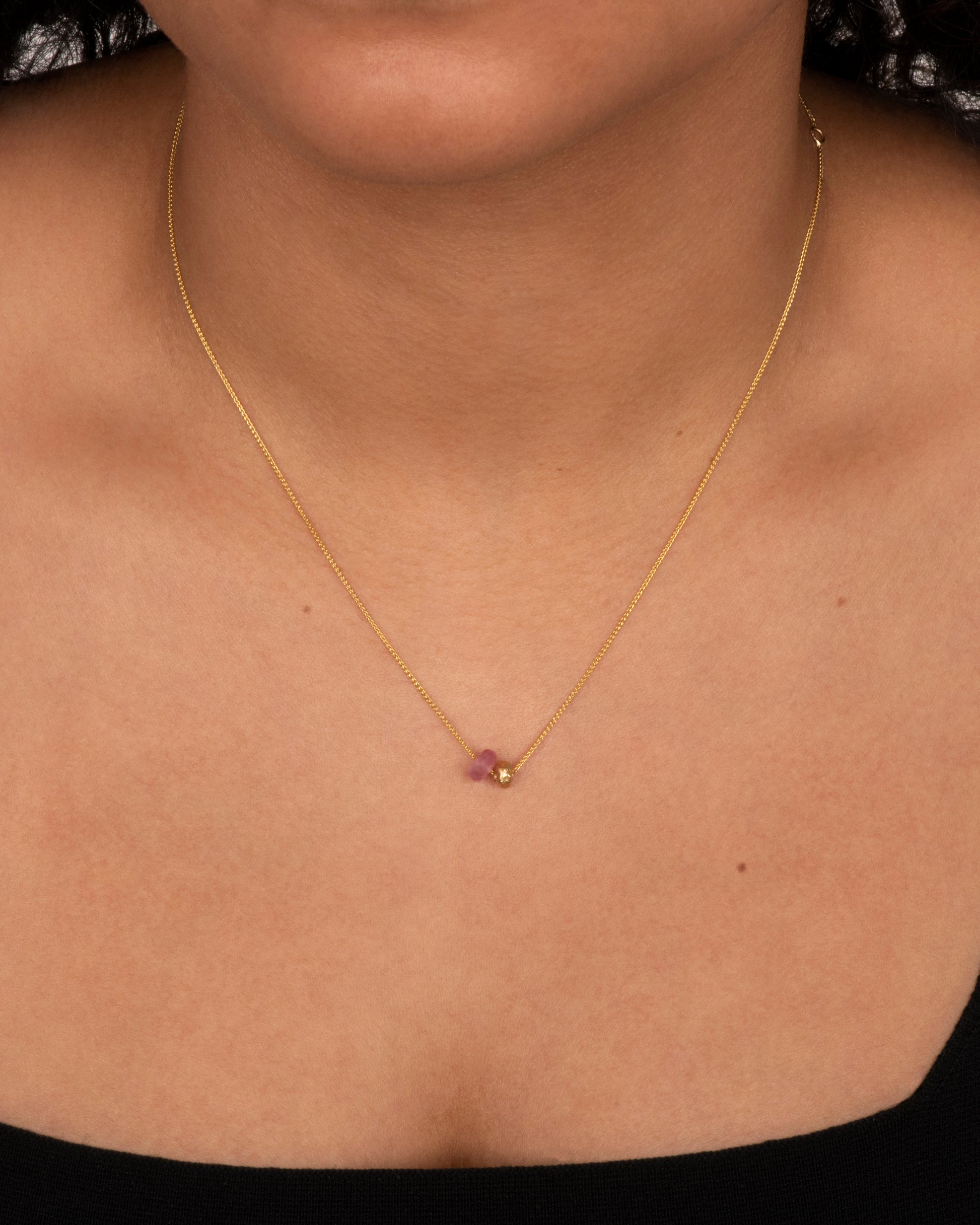 A pink tourmaline bead and gold textured bead hang from a yellow gold chain. View on a neck.