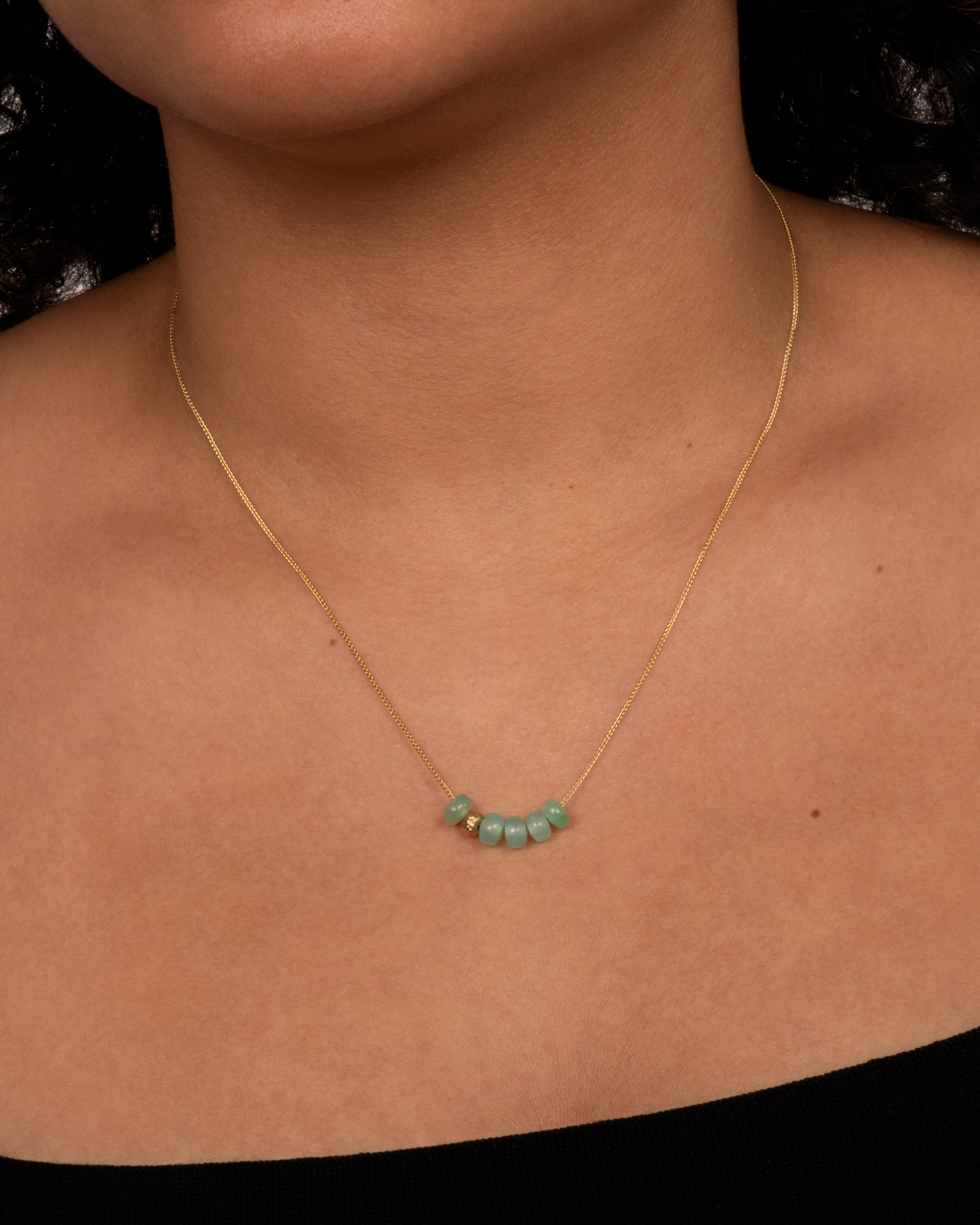 A yellow gold necklace with six beads, five of them chrysoprase and one of them textured gold. View on a neck.