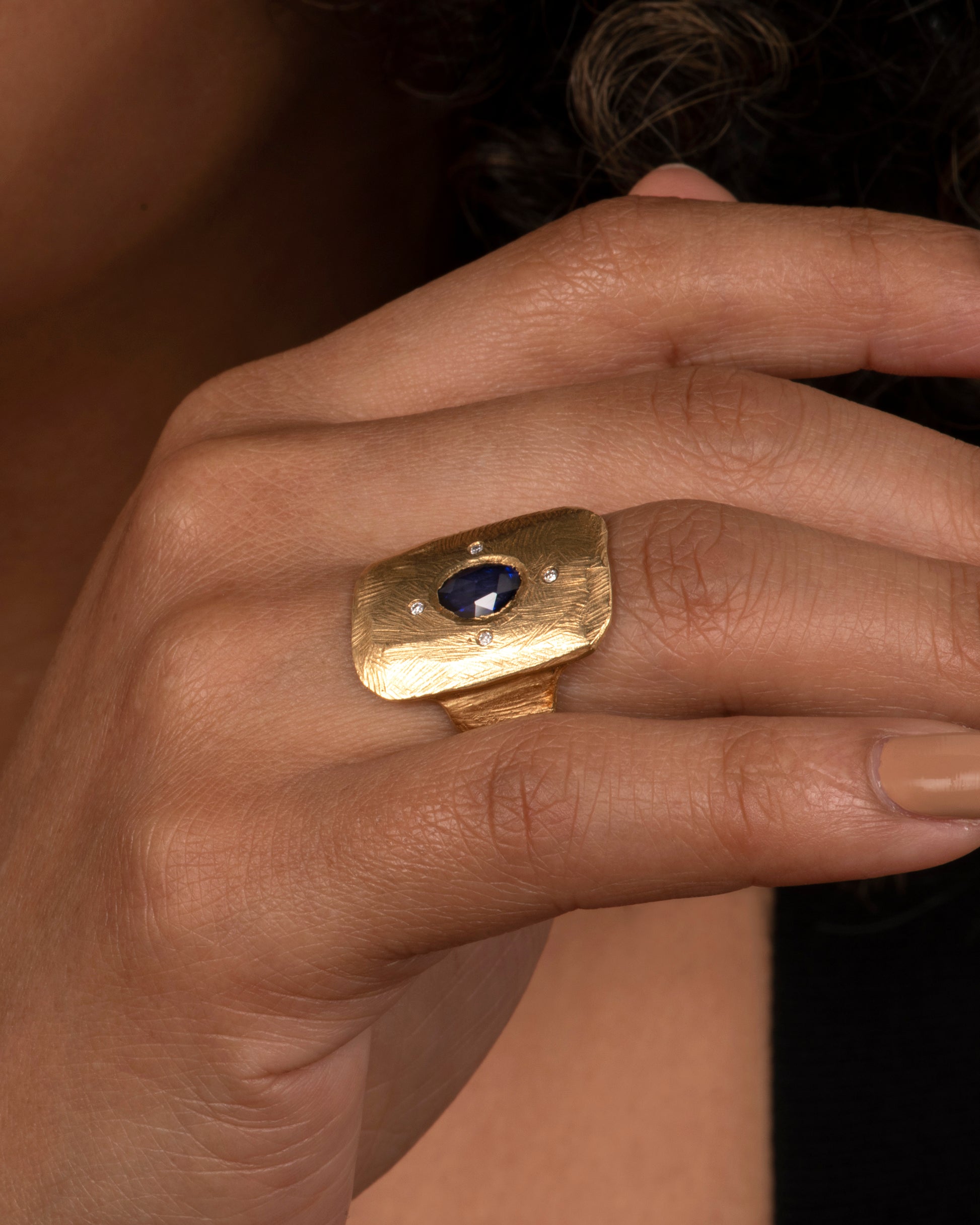 An 18k gold hand carved cocktail ring with a rose-cut, dark blue sapphire dotted with four star-like diamonds. Shown on hand.