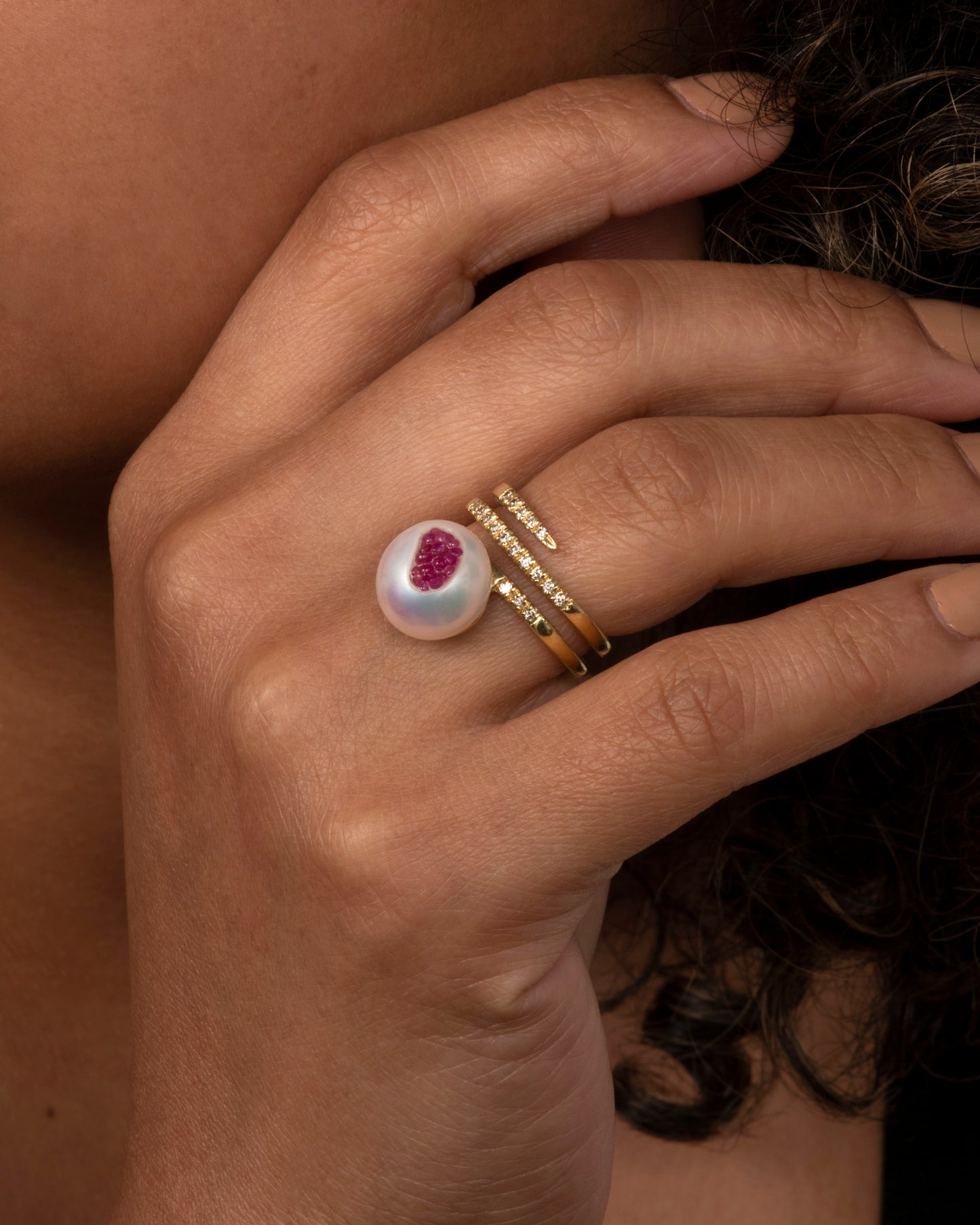 side view of a little h yellow gold wrap ring finished with an organic freshwater pearl that has been gutted and lined with rubies. Shown on hand.