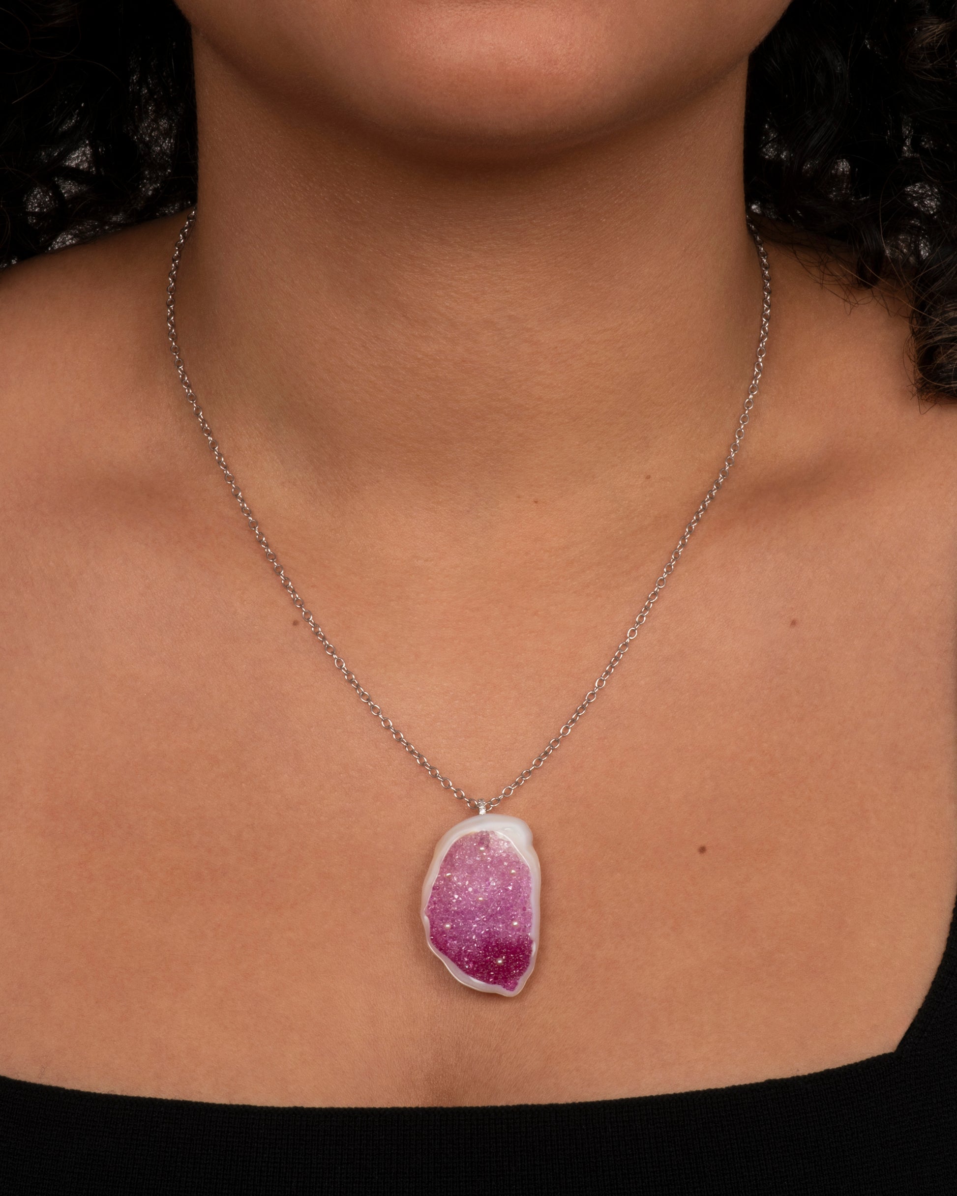 Close up side view of a large freshwater souffle pearl carved out and lined with ombre pink sapphires on a pendant with seed pearl accents. View from the front on a neck.