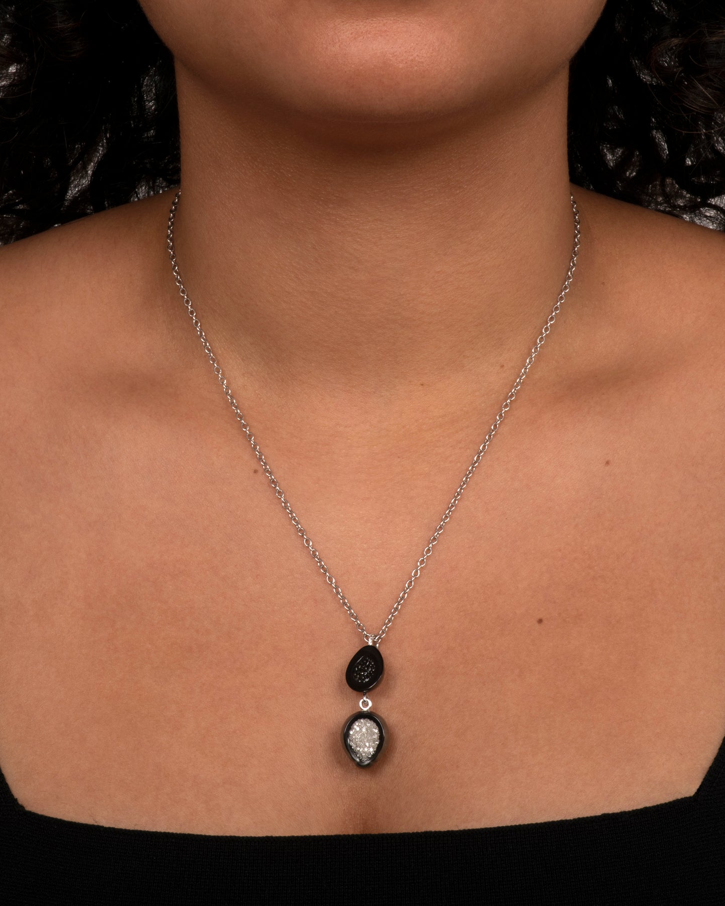 A white gold necklace with a double tiered Tahitian pearl pendant lined with black and white diamonds and a pave diamond bail. View on a neck.