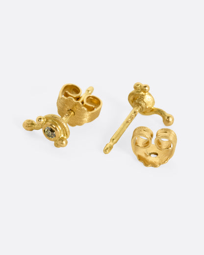 A pair of yellow gold drip stud earrings with green diamonds, shown from the side with one earring open.