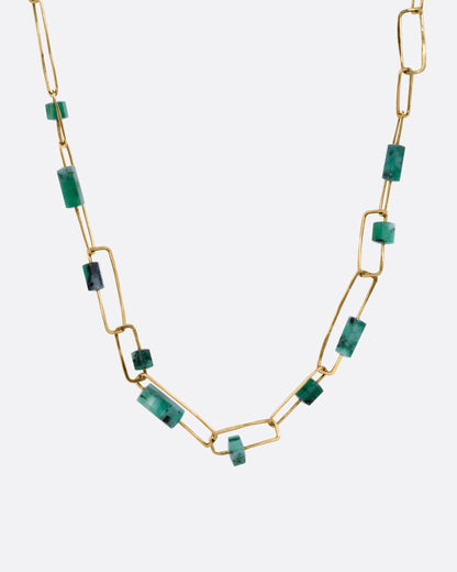 A yellow gold paperclip chain necklace with emerald beads, shown from the front.