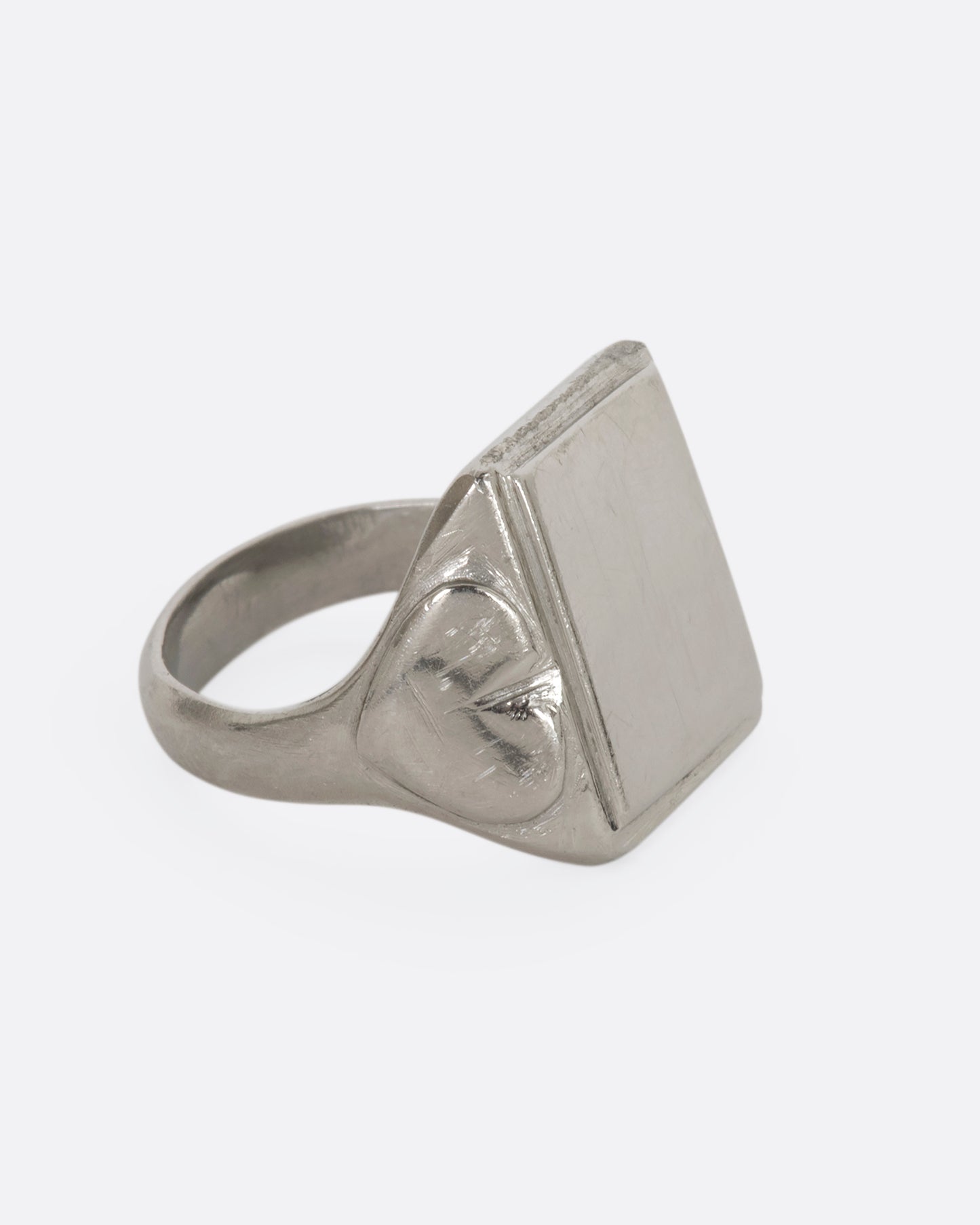 A white gold blank square signet with heart-like designs on the shoulders. View from the alternate side.