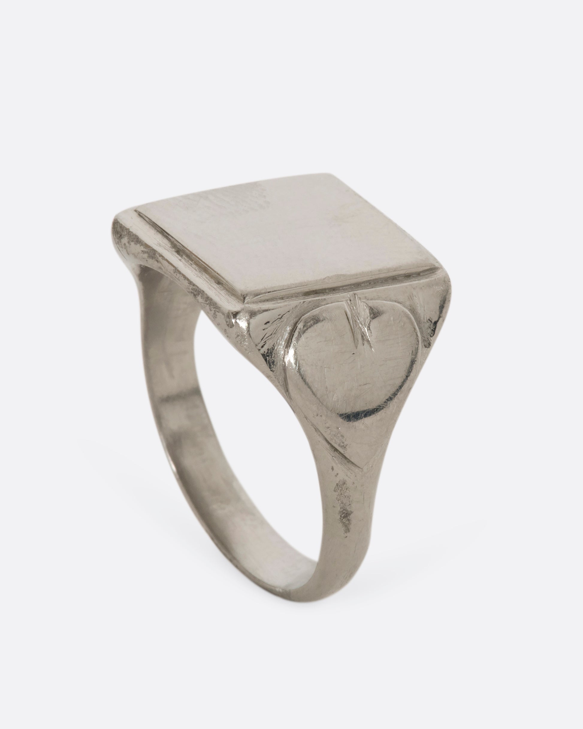 A white gold blank square signet with heart-like designs on the shoulders. View from the side standing up.