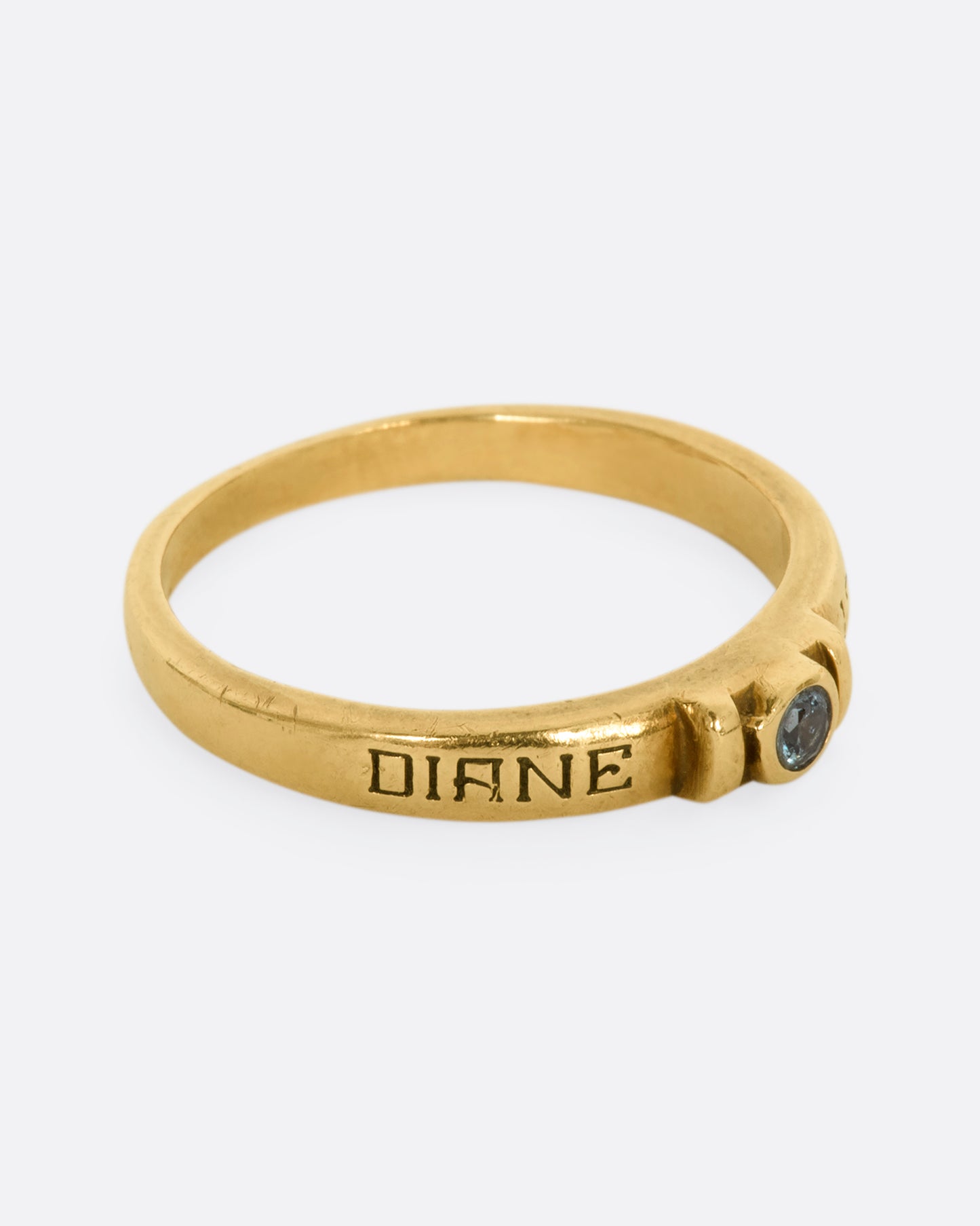 A yellow gold engraved band with a round blue topaz stone at the center. View from the side.