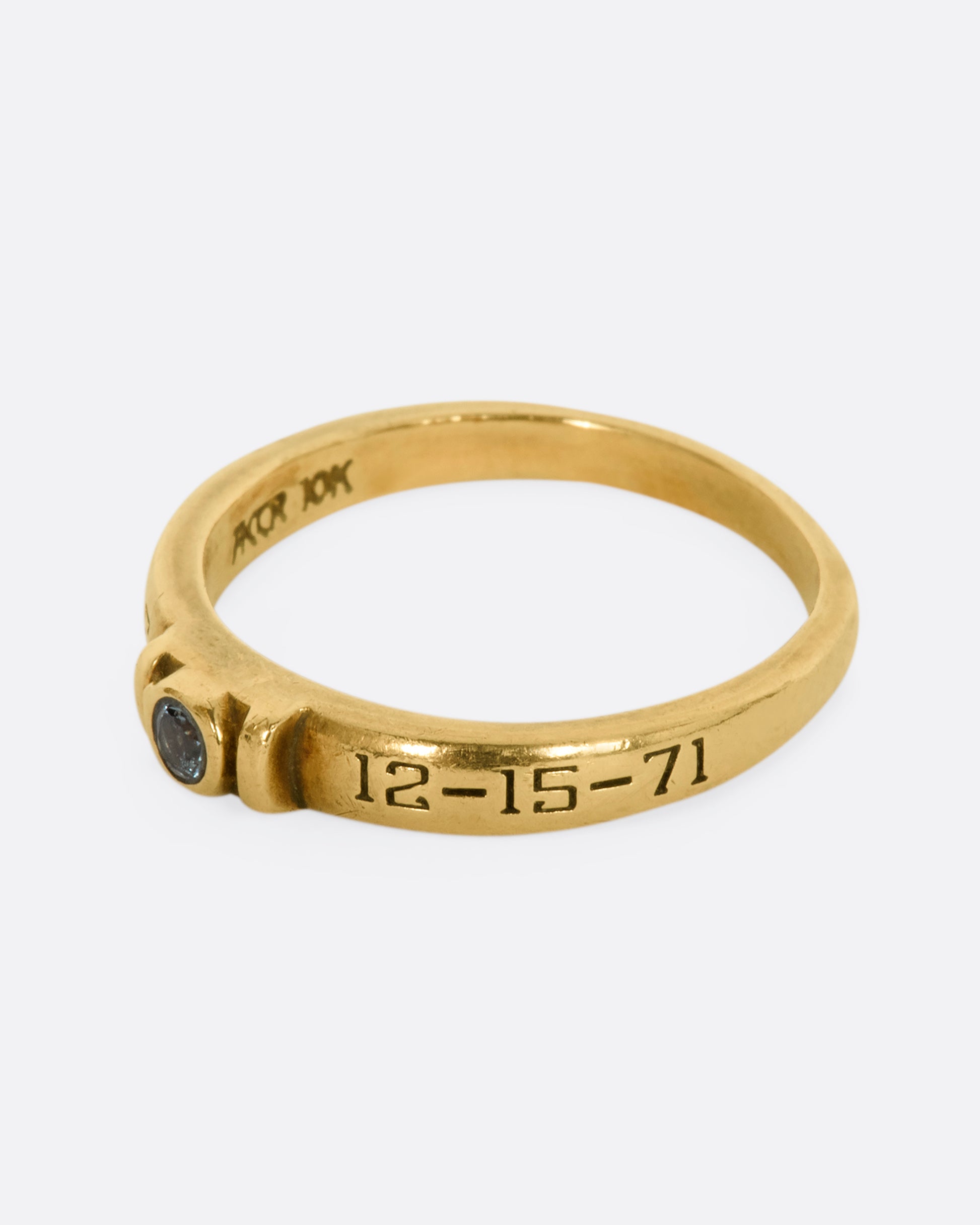 A yellow gold engraved band with a round blue topaz stone at the center. View from the side.