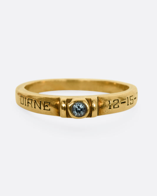 A yellow gold engraved band with a round blue topaz stone at the center. View from the front.