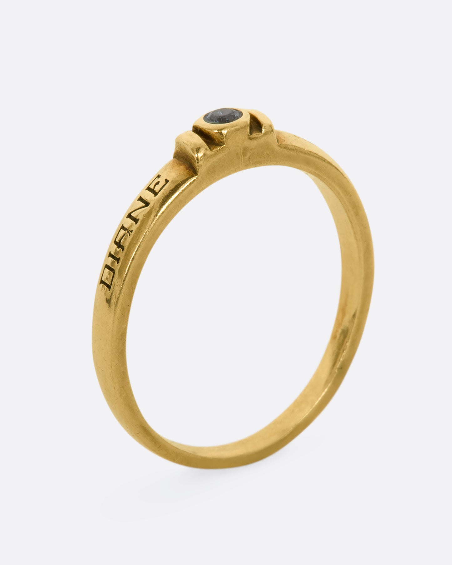 A yellow gold engraved band with a round blue topaz stone at the center. View standing up from the side.