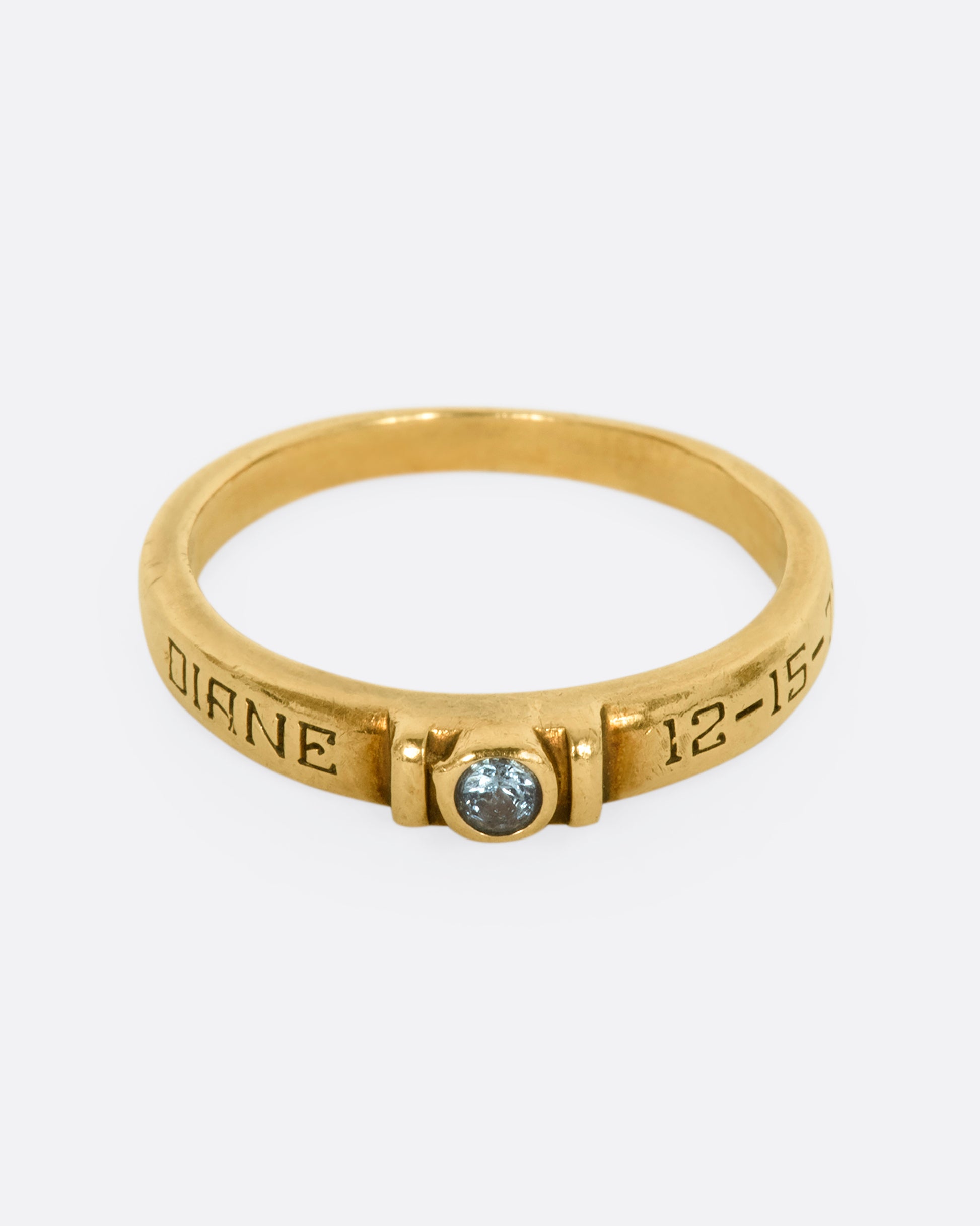 A yellow gold engraved band with a round blue topaz stone at the center. View from the front.