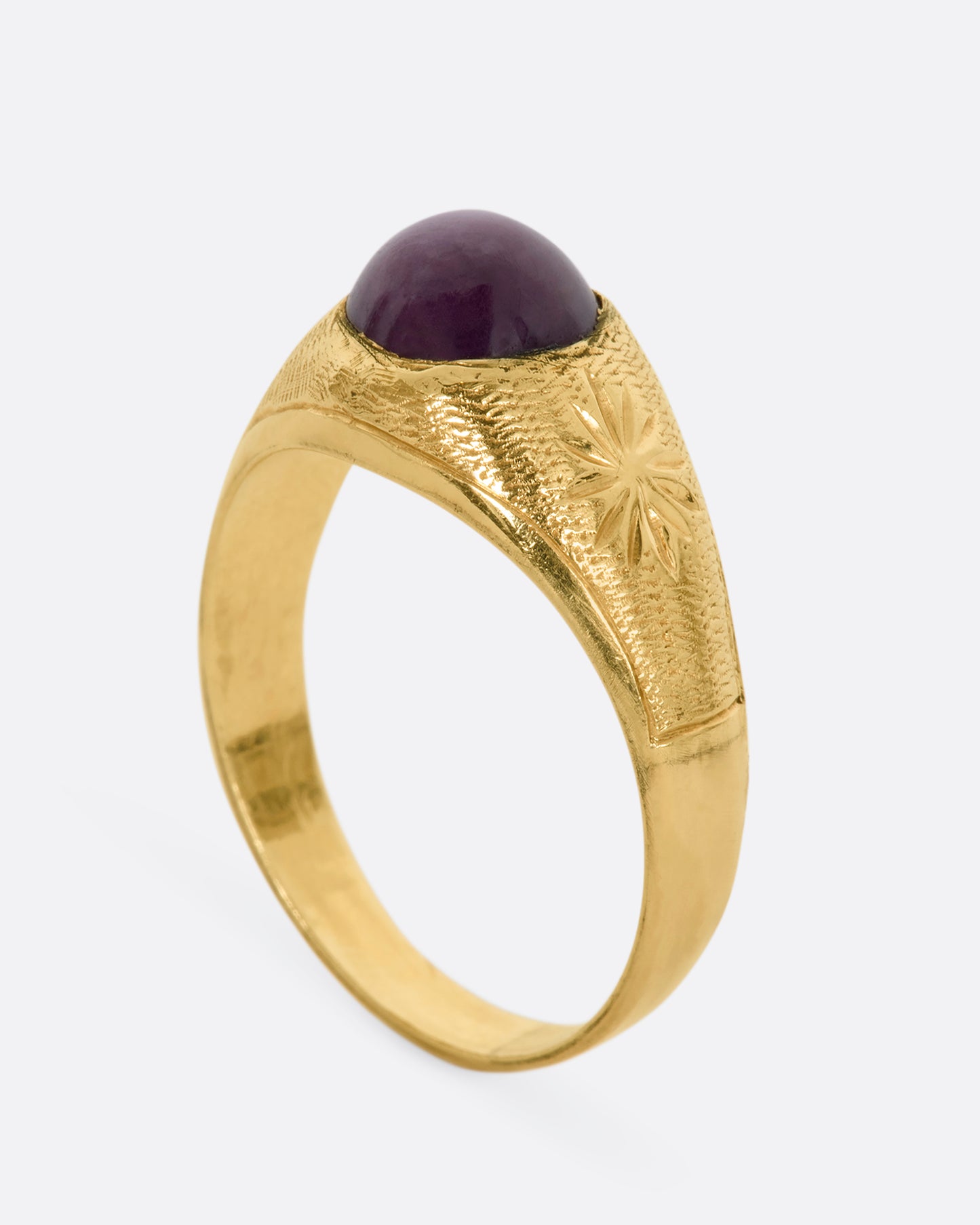 A domed yellow gold vintage ring with a ruby cabochon and starflower details. View from the side, standing up.