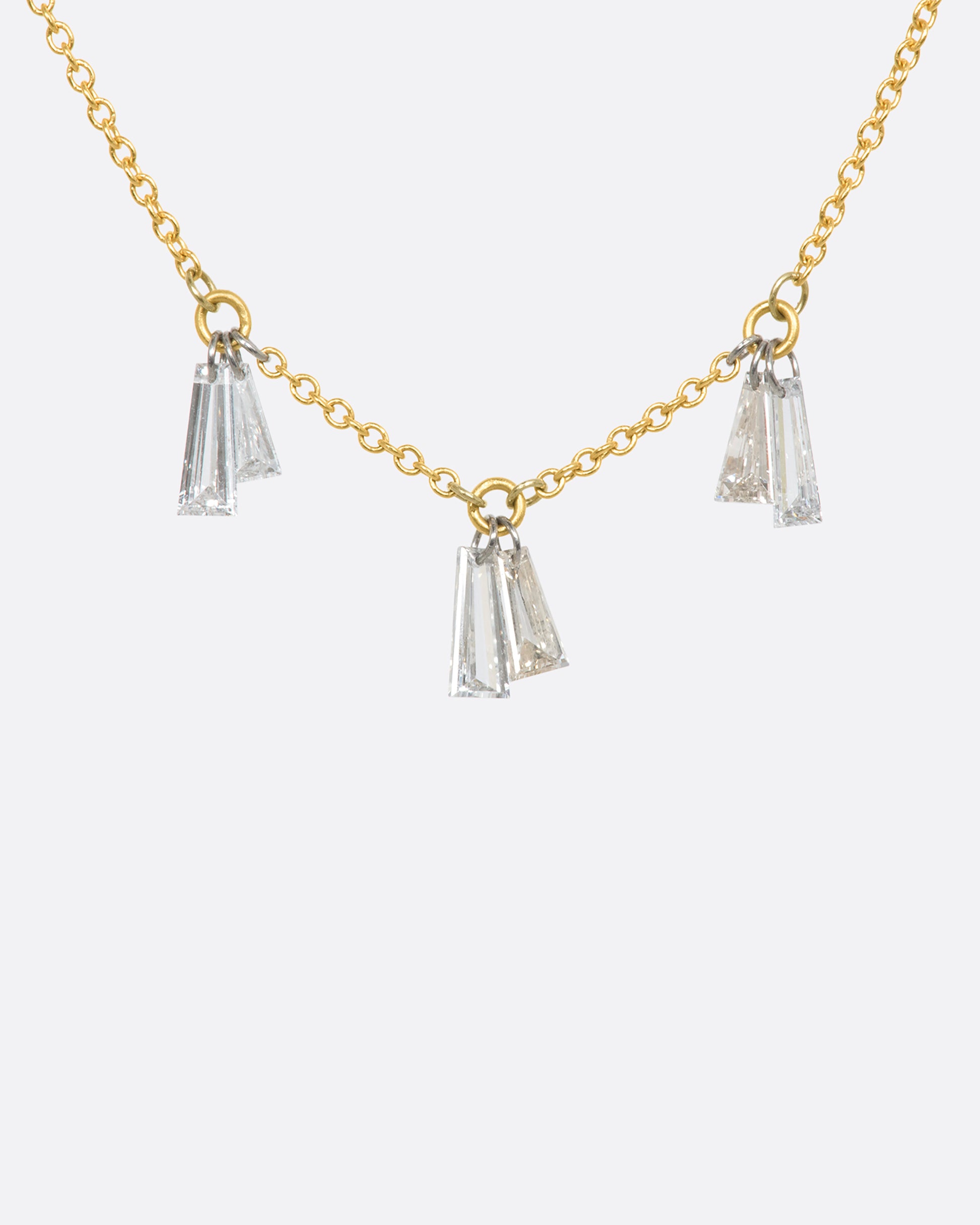 A yellow gold cable chain necklace with six baguettes hanging on platinum jump rings. View from the front.