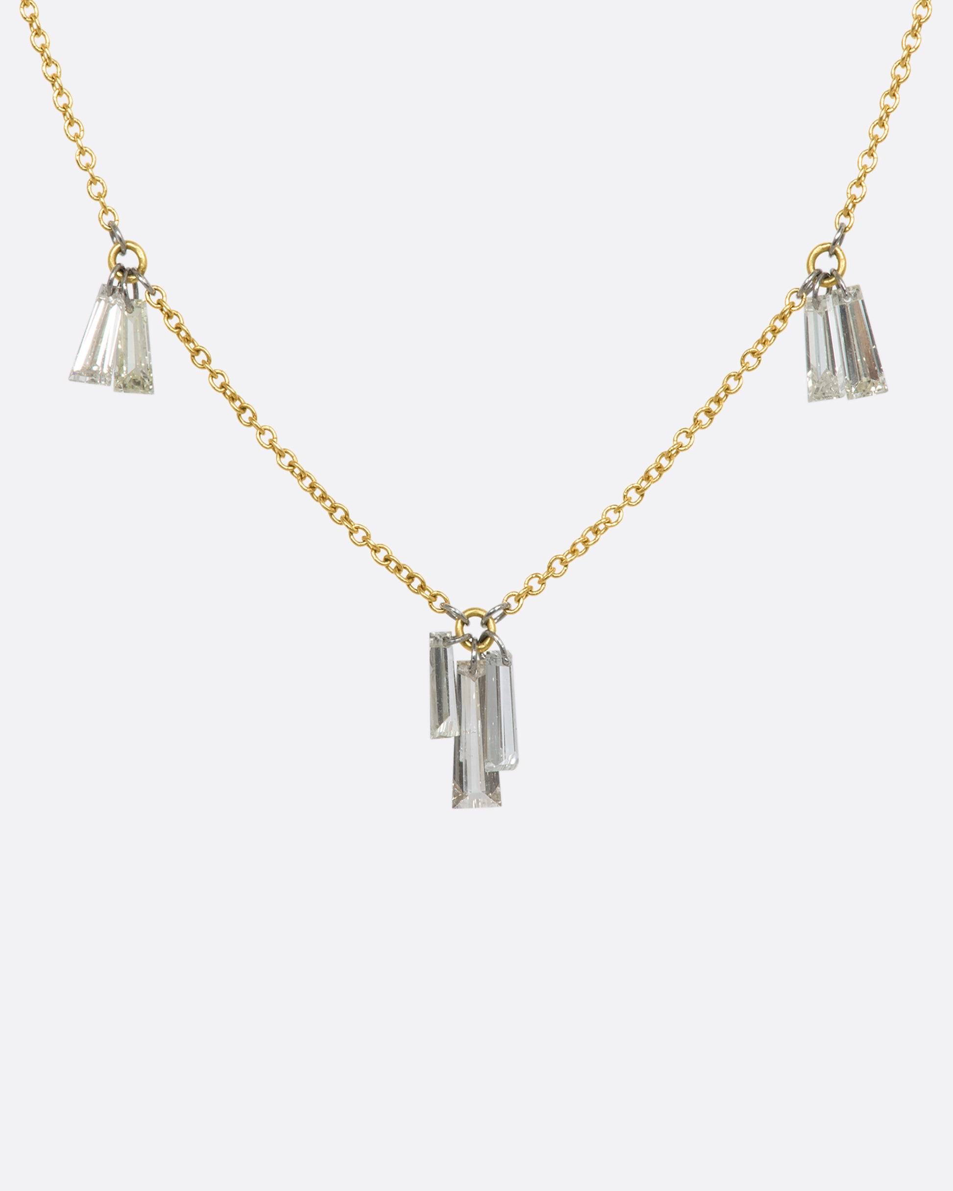 A yellow gold cable chain necklace with seven baguette diamonds dangling on platinum jump rings. View from the front.