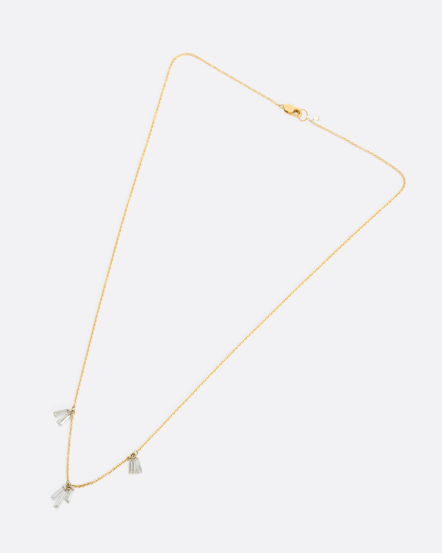 A yellow gold cable chain necklace with seven baguette diamonds dangling on platinum jump rings. View laying flat.