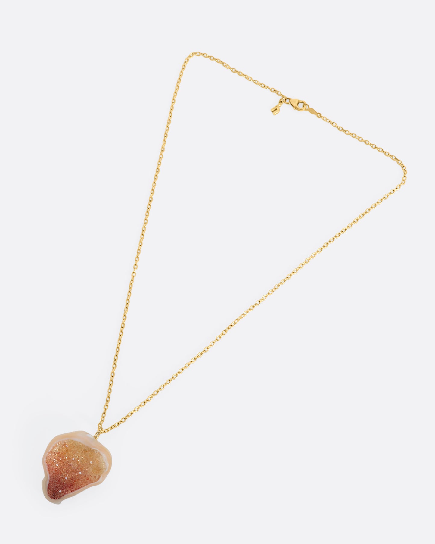 A yellow gold necklace with a soufflé pearl pendant lined with gradient orange sapphires and a pave diamond bail. View of the entire necklace laying flat.